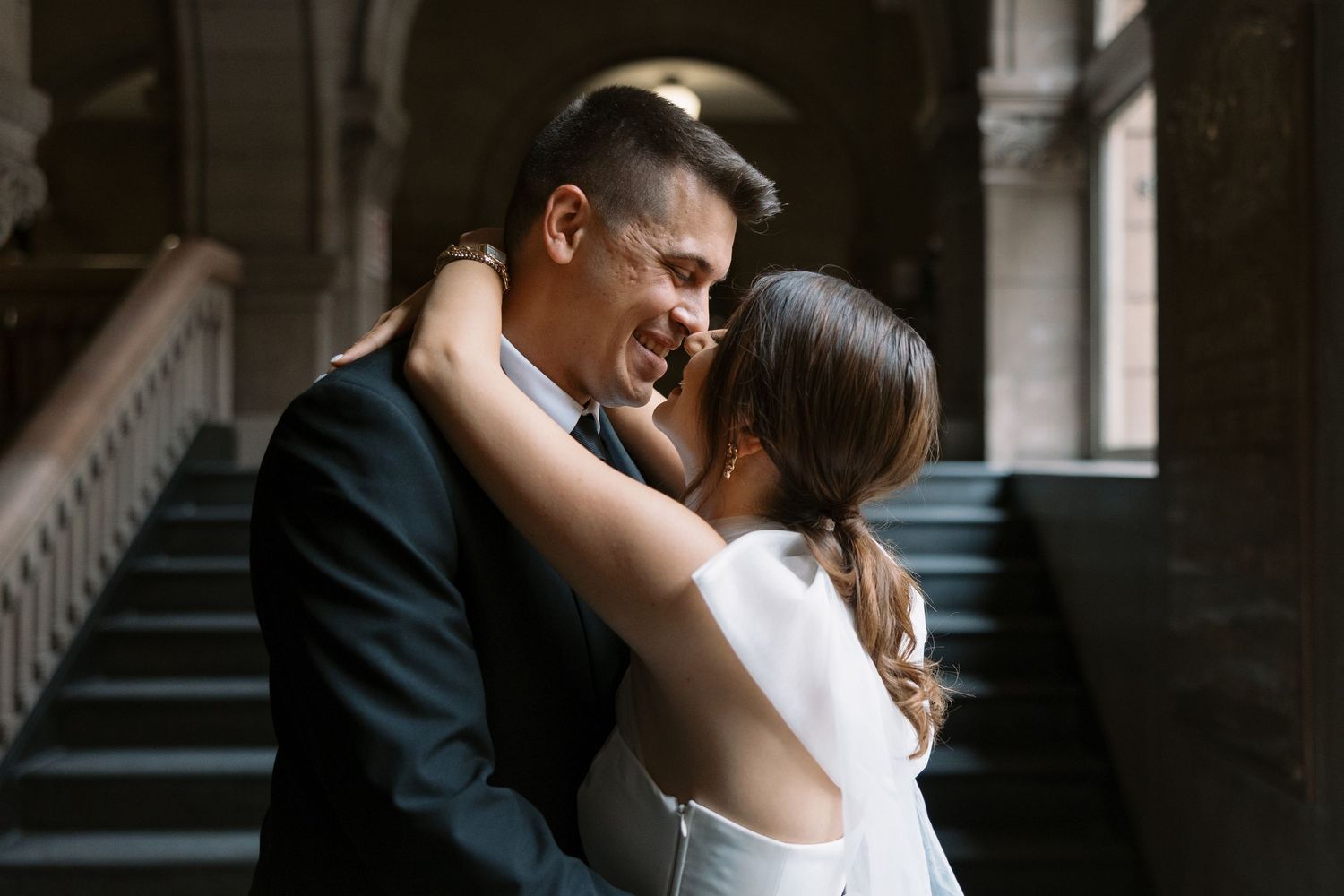 An intimate moment between a couple in formal attire beneath arched architecture.