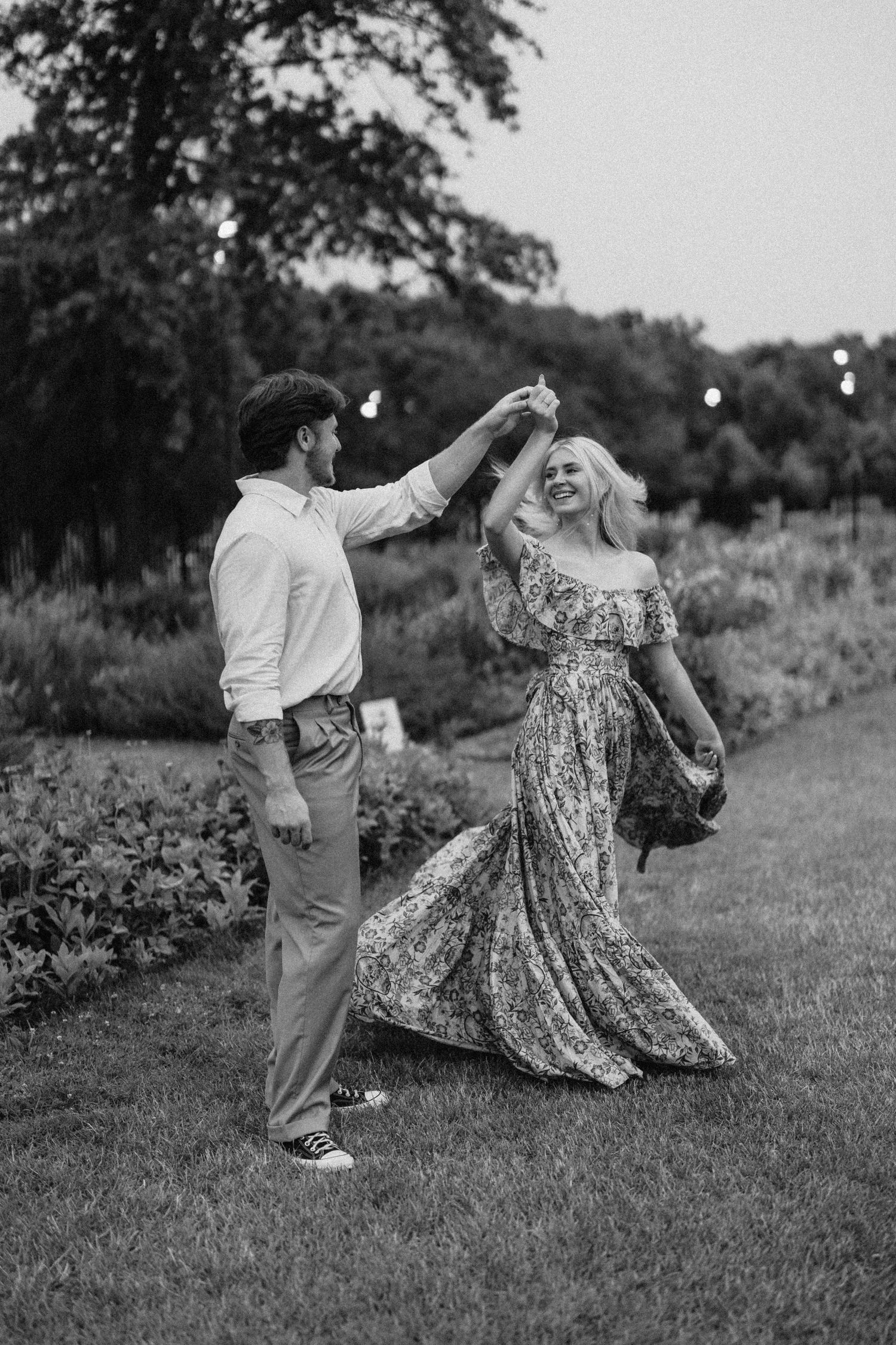 Couple dances joyfully on garden path in black and white photograph.