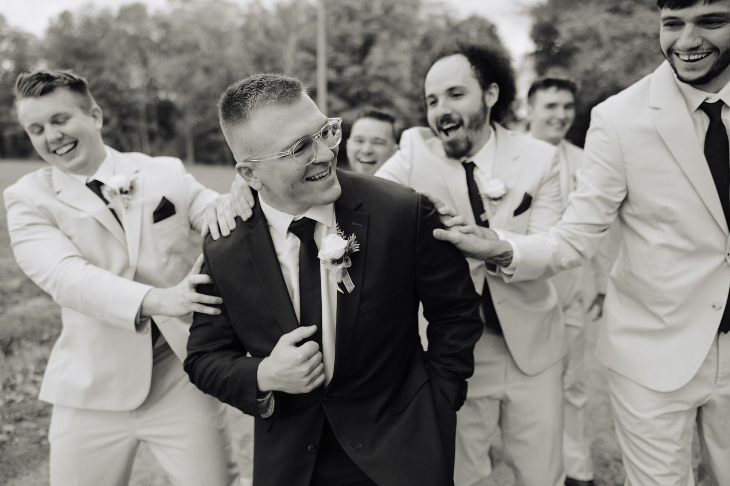 Black and white photo of groomsmen laughing with groom in candid moment.