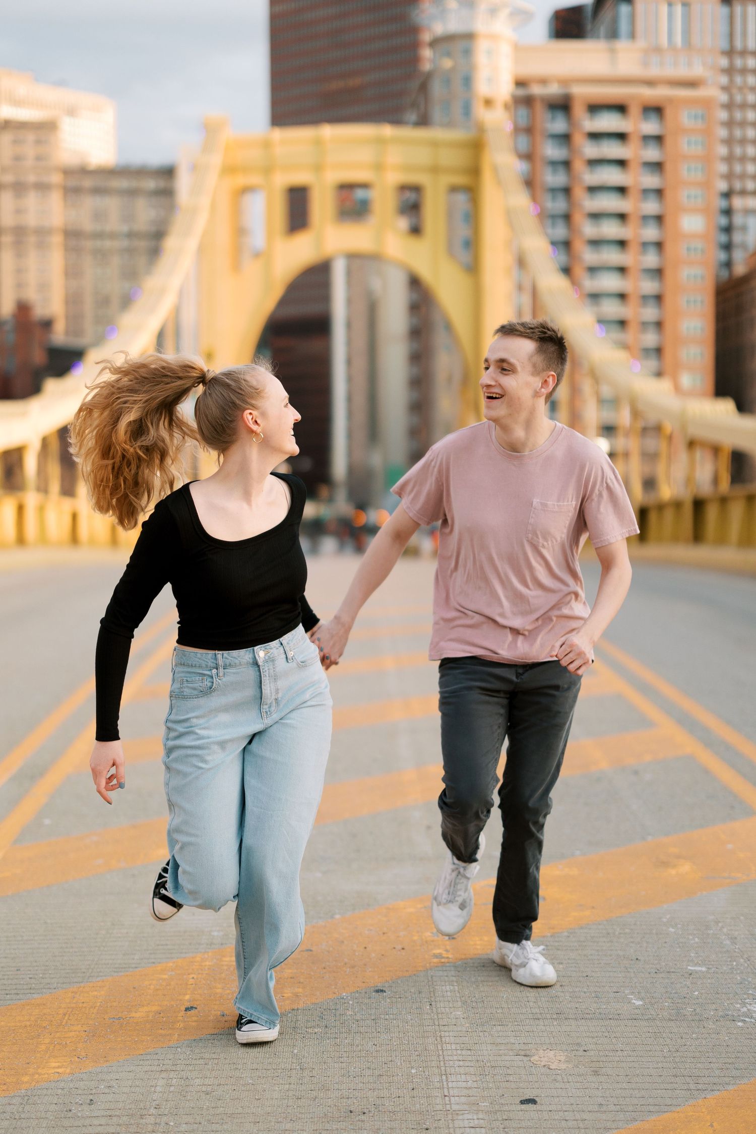 A playful couple running and laughing on a yellow bridge with city buildings behind them.