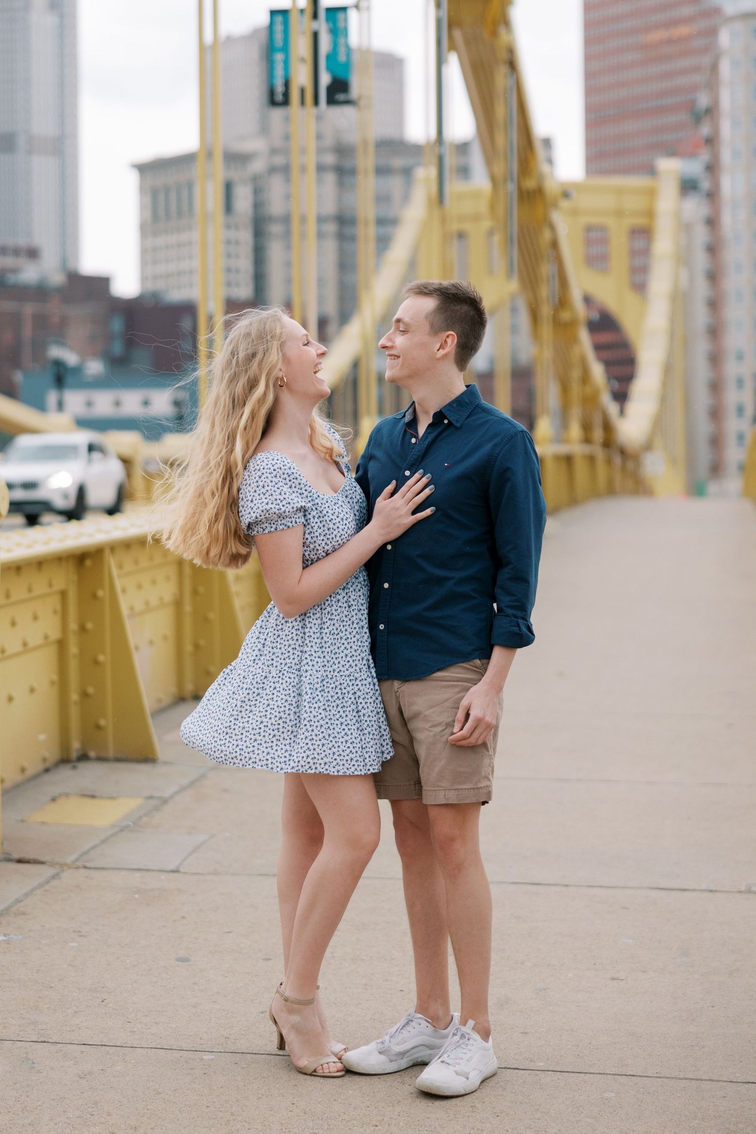 Couple shares romantic moment on yellow bridge with city skyline backdrop.