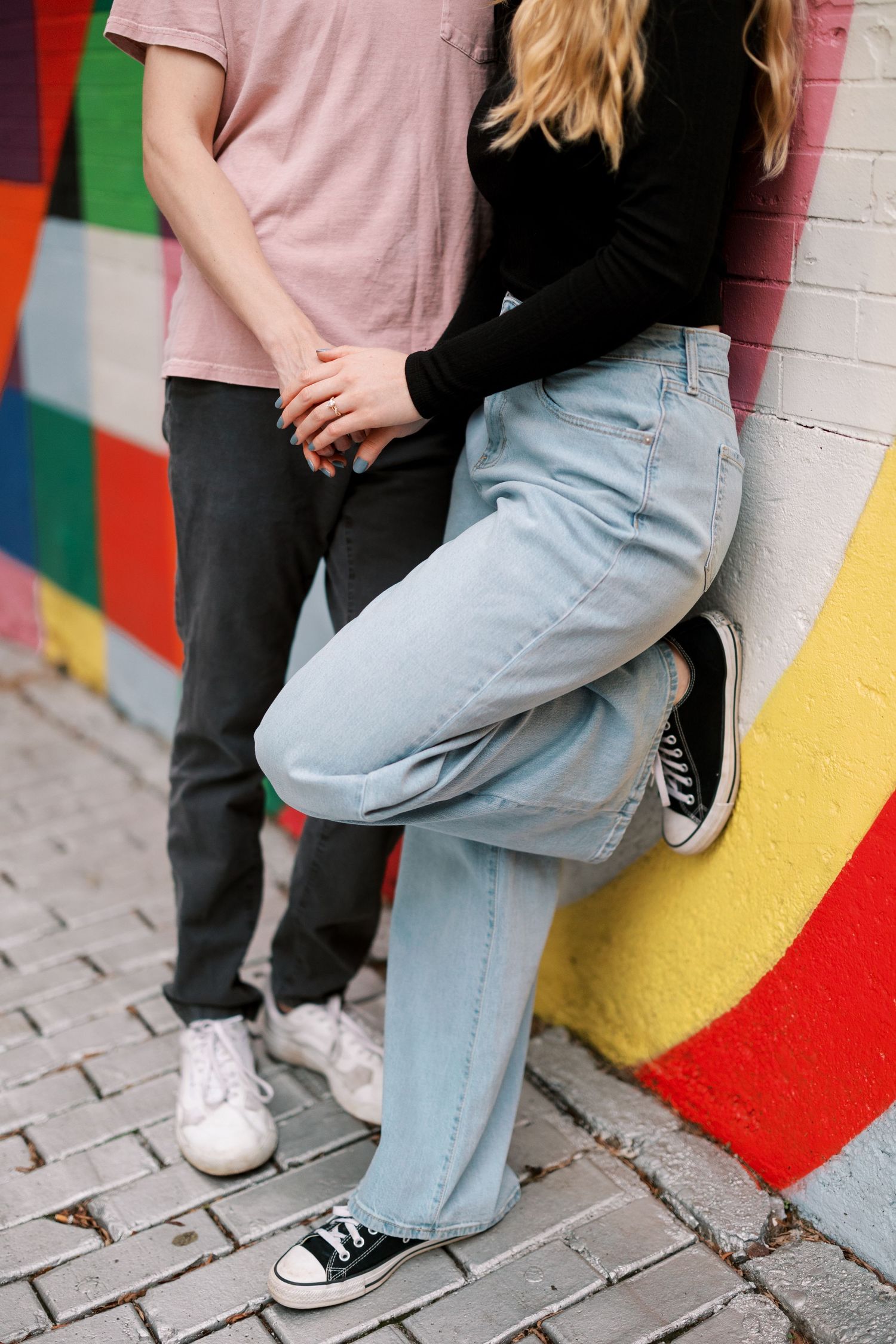 A couple in casual wear holding hands against a colorful geometric mural wall.