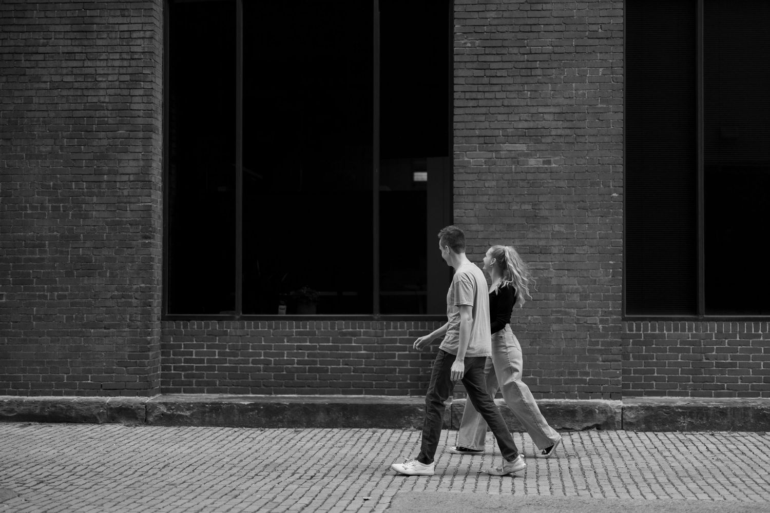 A black and white image of two people walking together on a brick sidewalk.