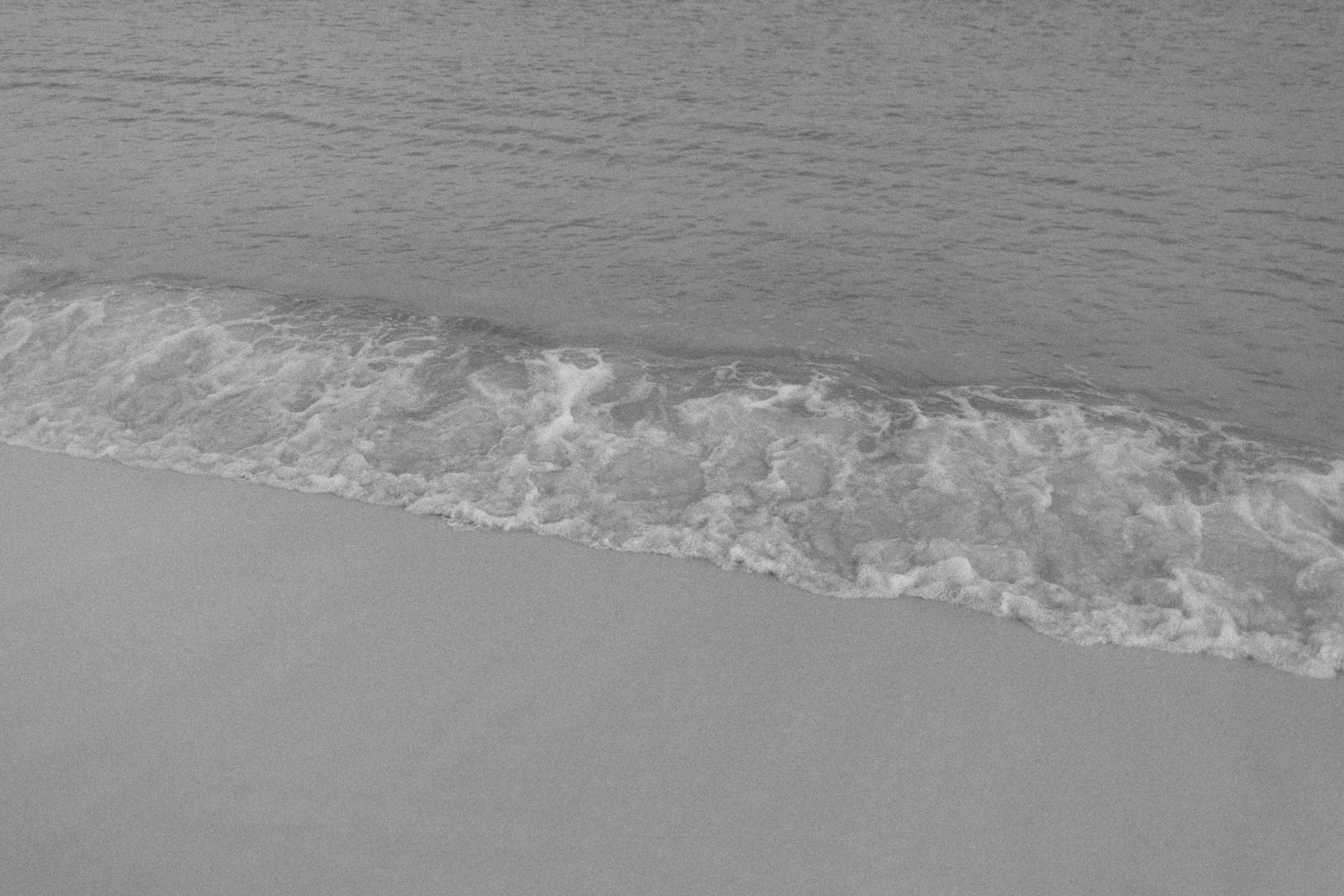 Minimalist black and white photograph of waves washing up on a sandy beach.