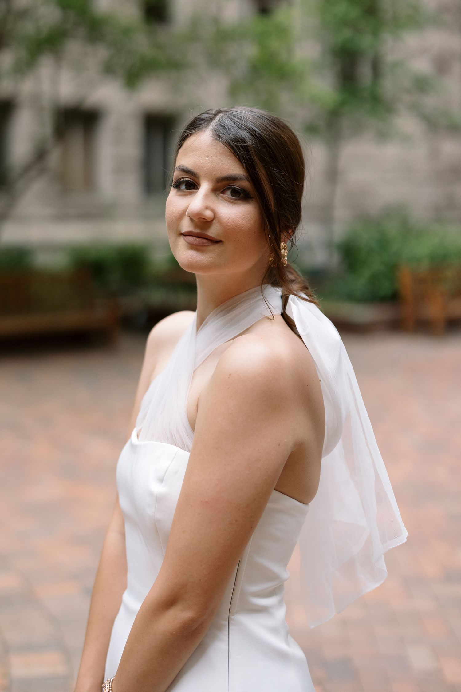 A side-angle portrait of a bride wearing a sleek white halter dress and veil.