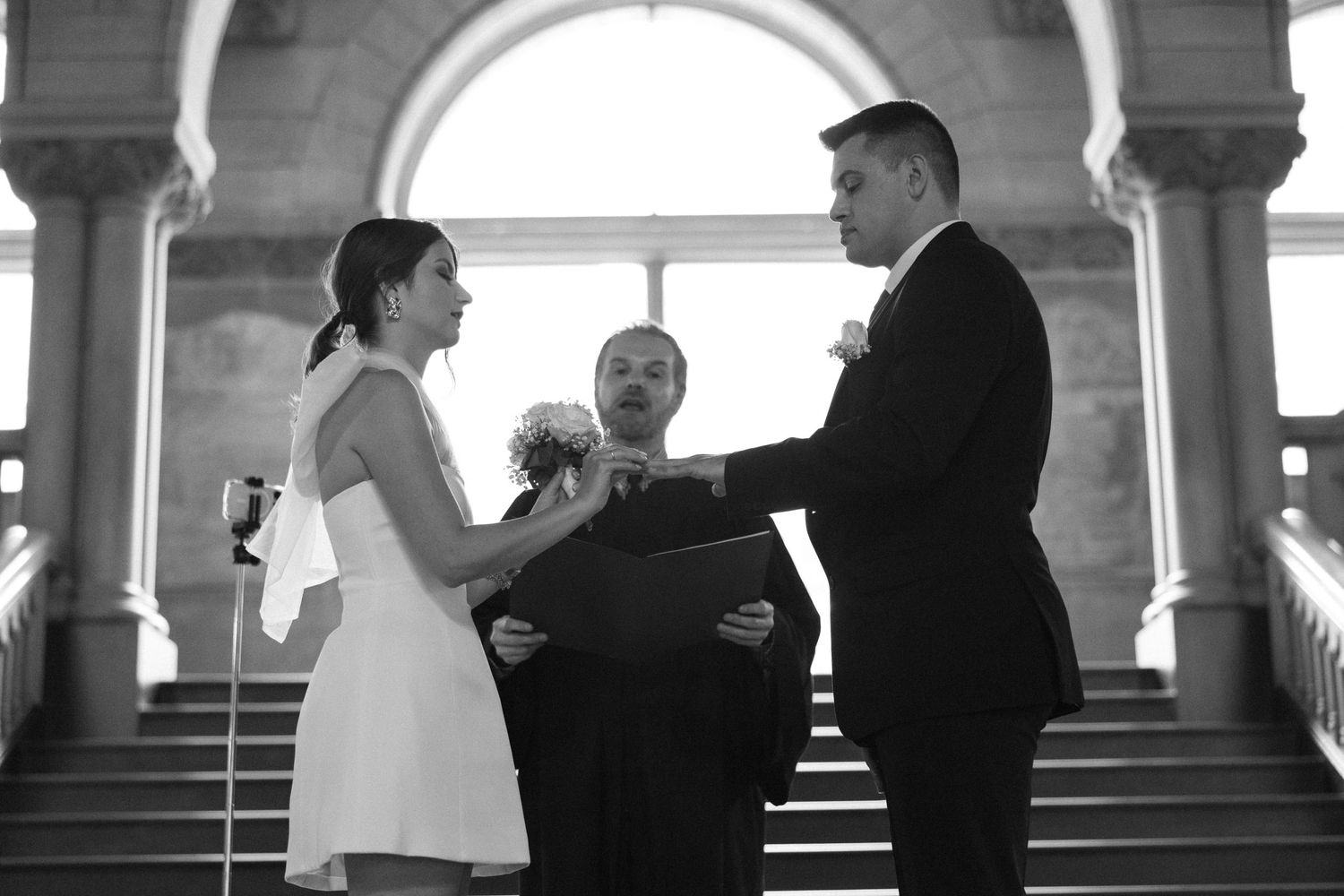 A wedding ceremony takes place under elegant stone archways with a couple exchanging vows.