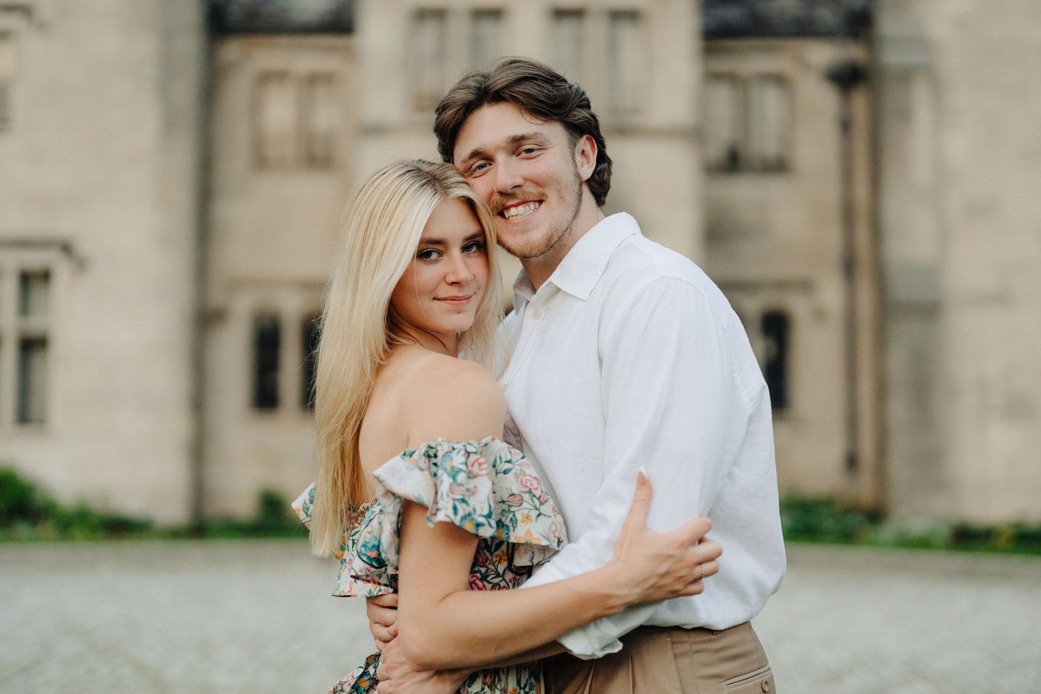 Happy couple shares warm embrace outside classic stone mansion.