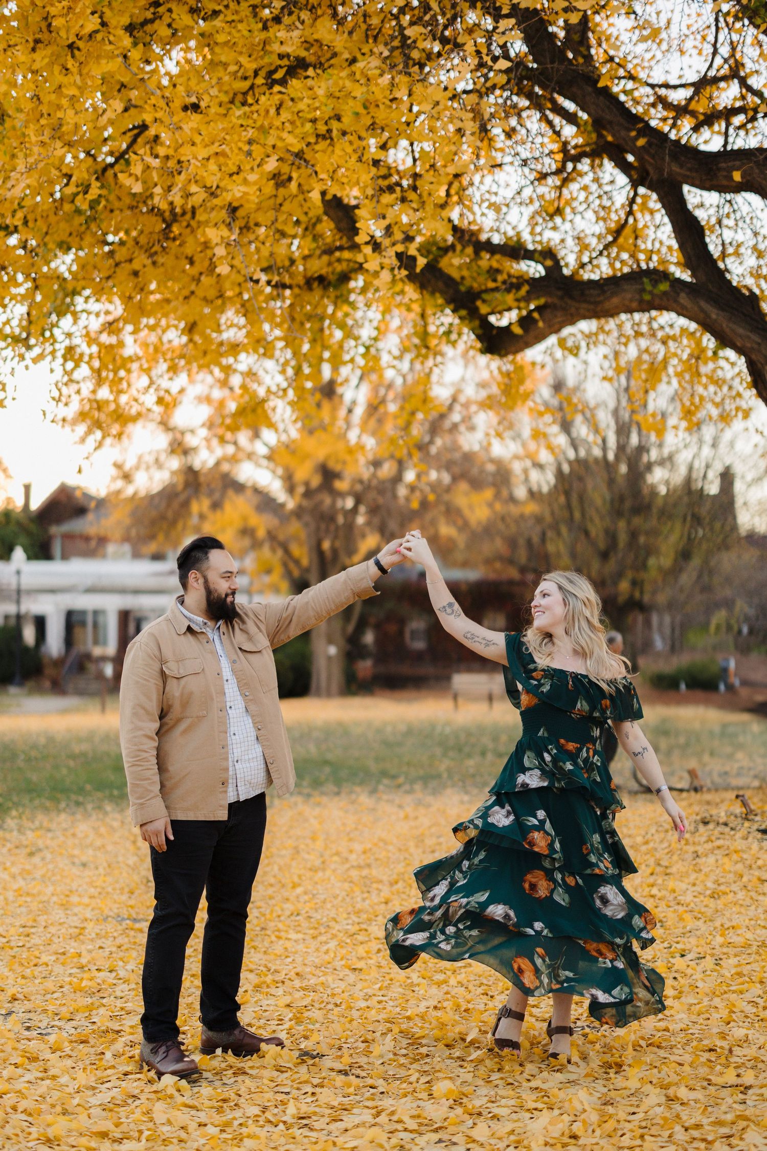A couple dances and plays in a park covered with vibrant yellow fall leaves under golden trees.