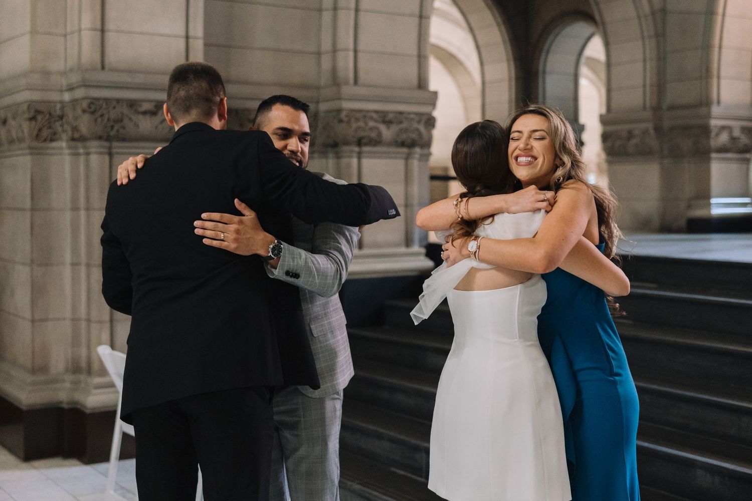 Group hug celebration in formal attire beneath historic stone architecture.