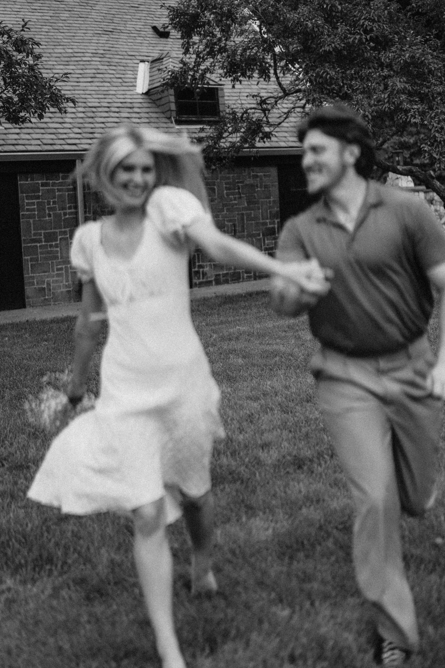 A black and white capture of a carefree dance moment on a lawn near a brick building.