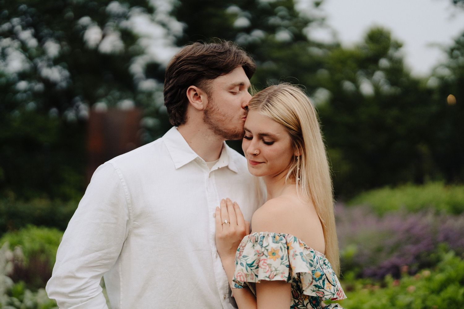 Romantic couple embraces in garden with blooming purple flowers in soft evening light.
