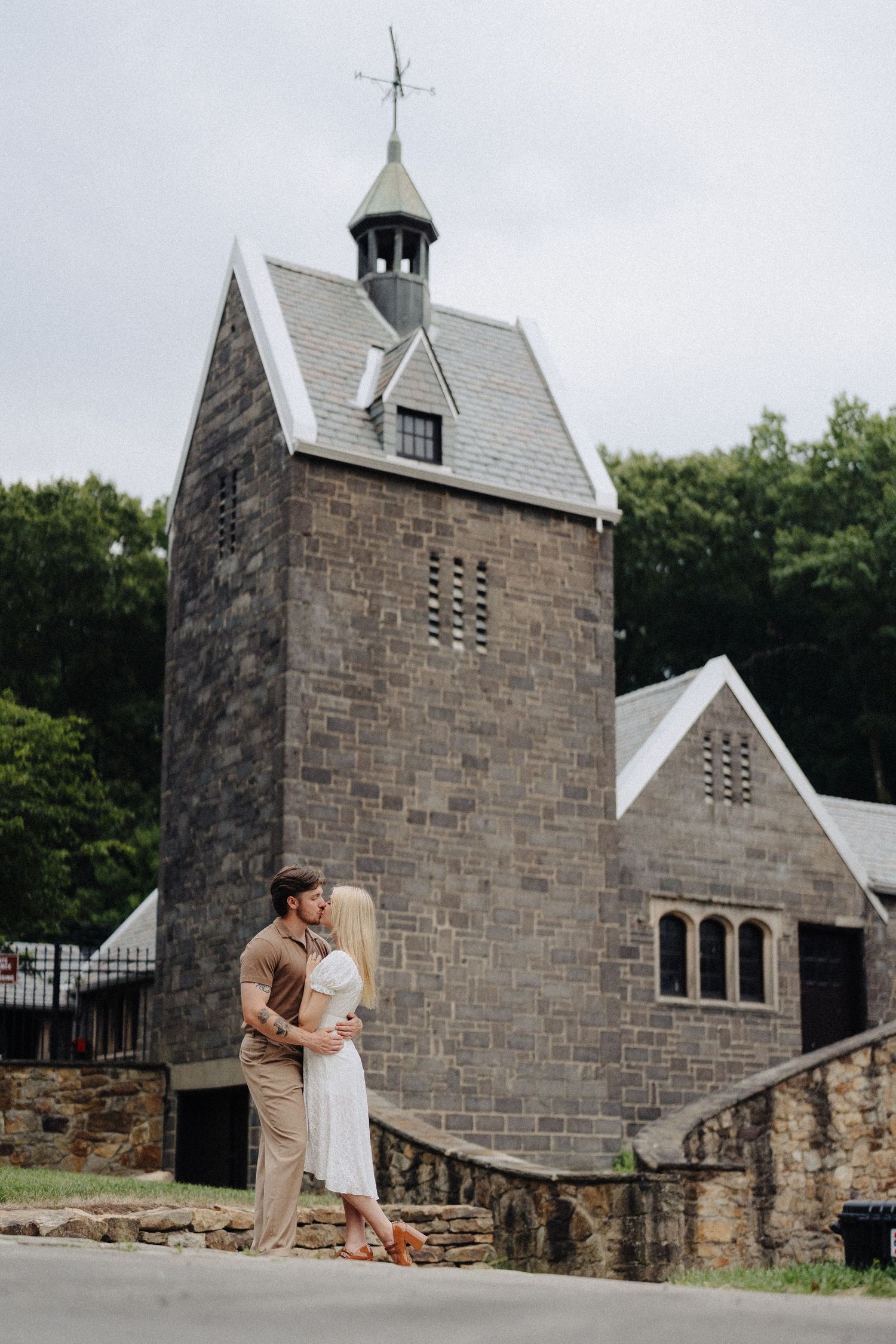 A couple shares an intimate moment in front of a stone church tower with unique architecture.