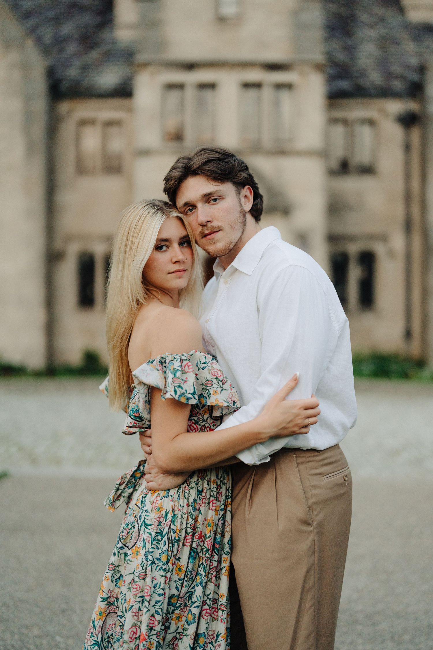 Elegant couple embraces in front of historic stone building during golden hour.