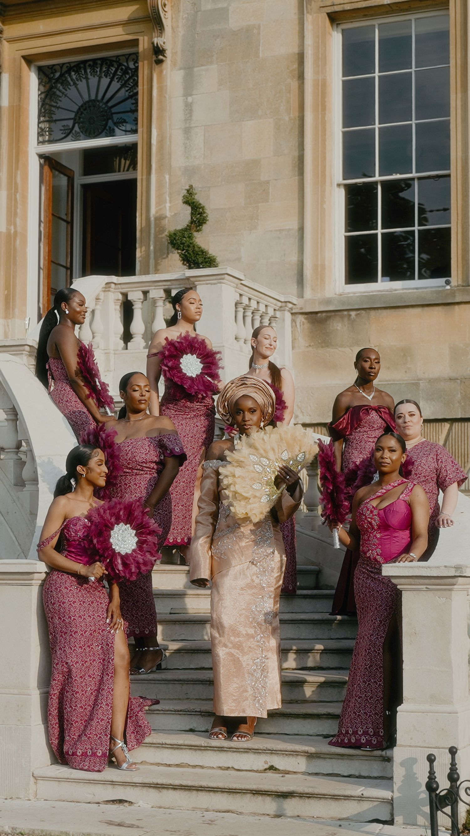 Wedding party wearing elegant burgundy sequined dresses poses on grand stone staircase of historic building.