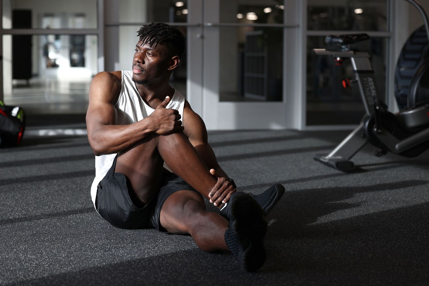 Athletic Black man resting on gym floor during workout session in modern fitness center.