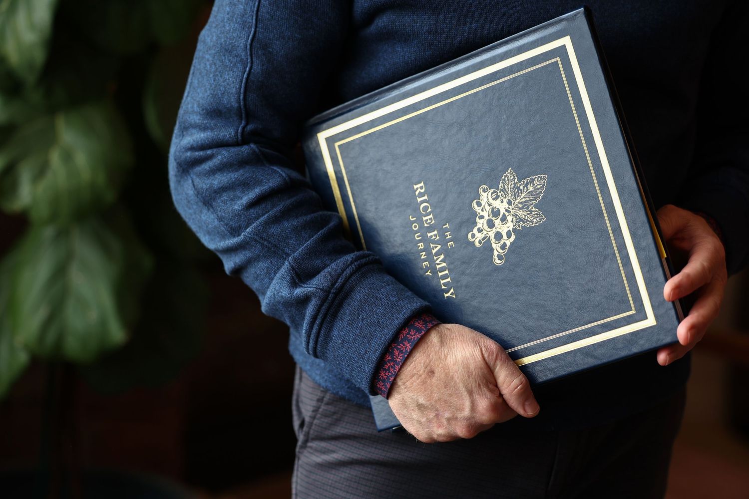 Person in blue sweater holding elegant navy Rice Family Journey hardcover book outdoors.