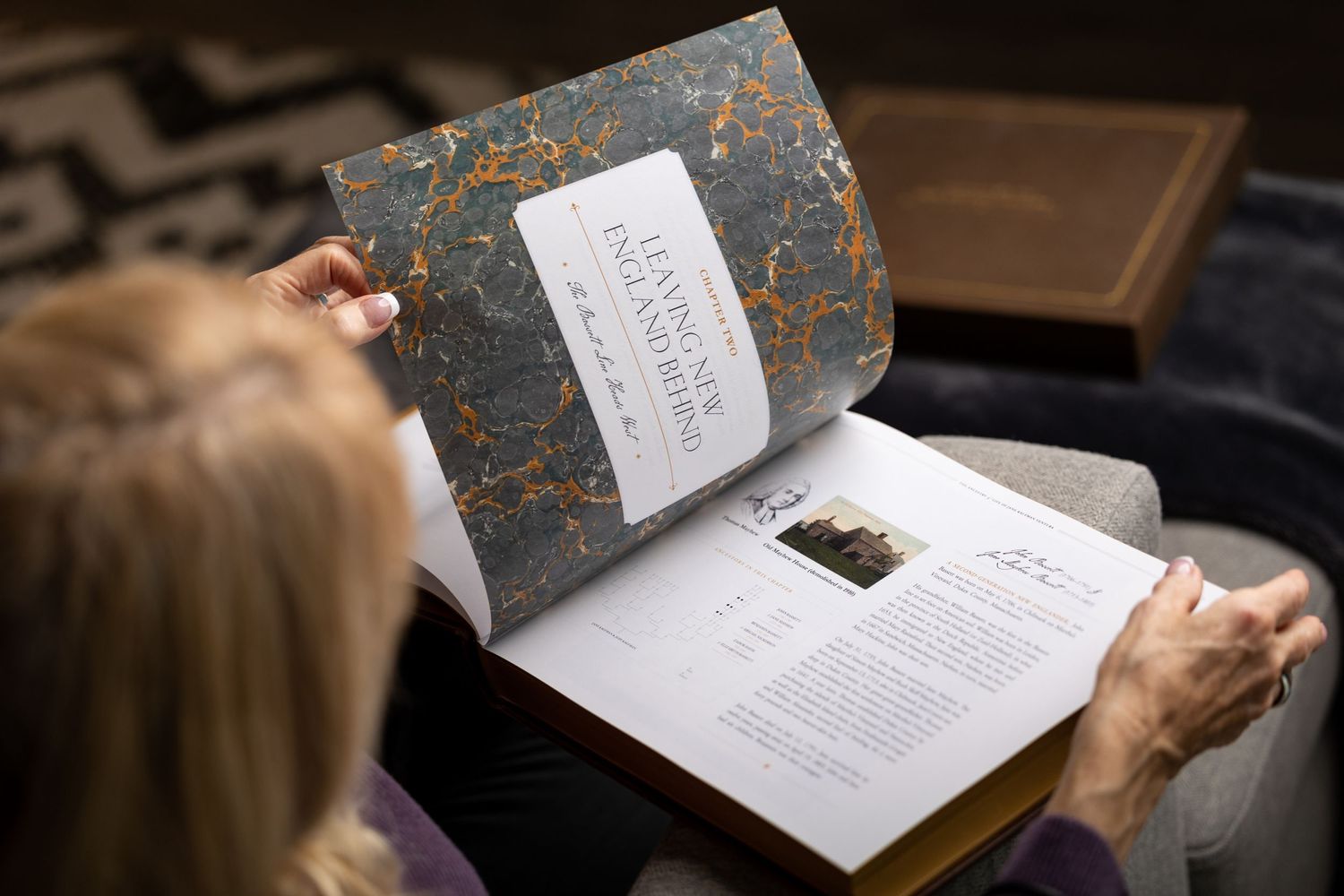 Woman reading open personalized family history book with marbled endpapers and vintage photos.