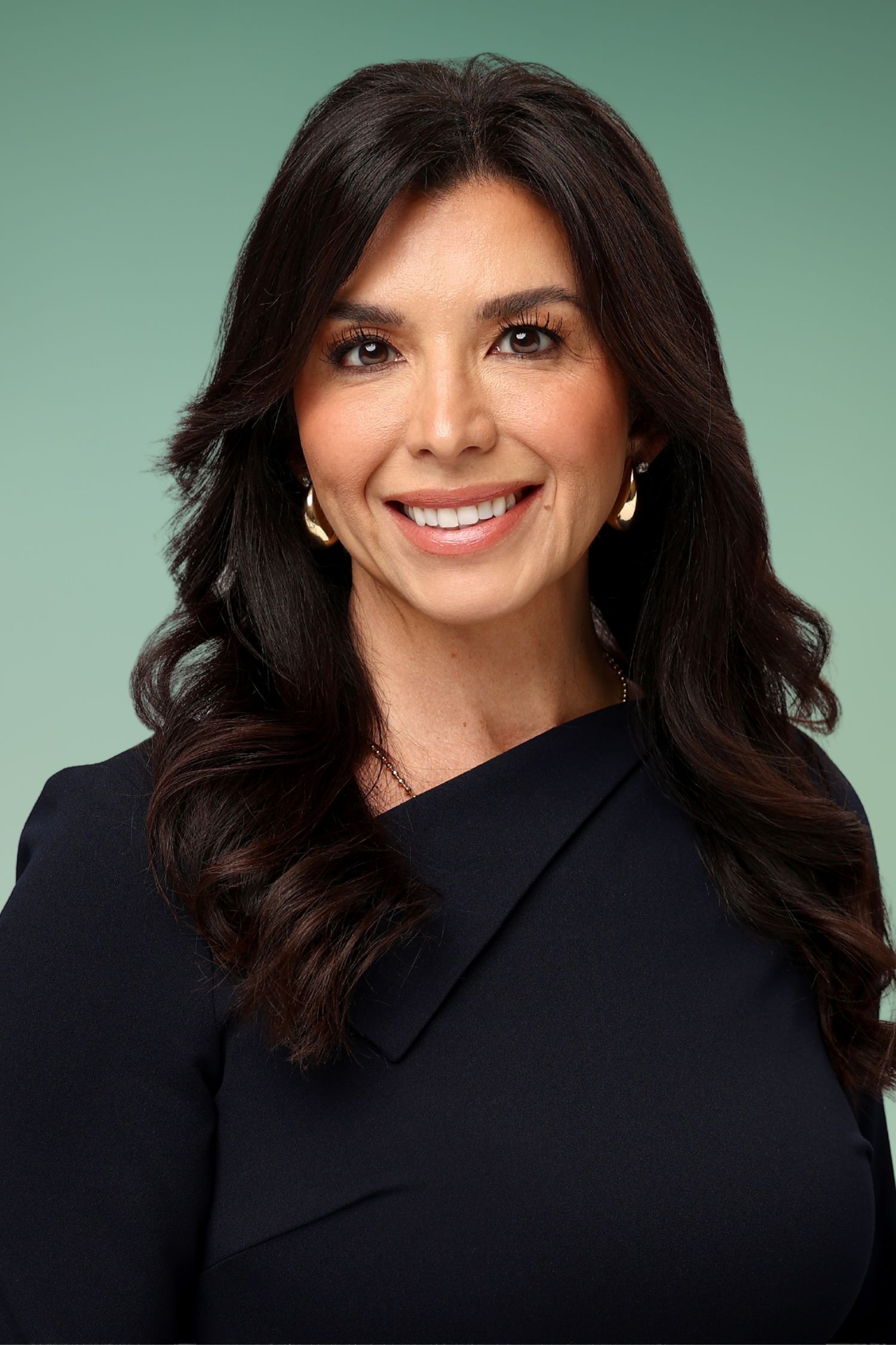 Professional headshot of a smiling woman with dark hair wearing a black blazer against a green background.