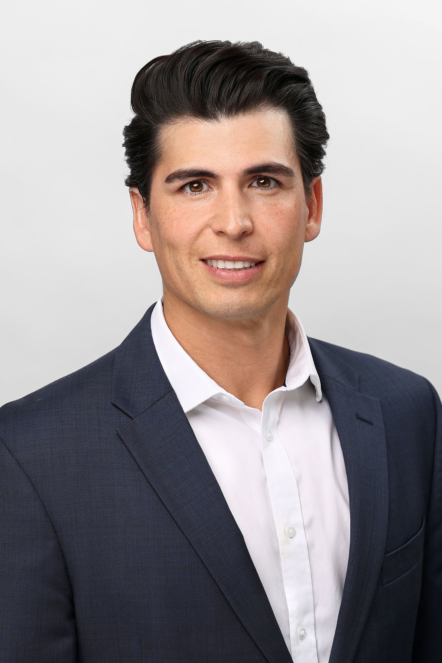Professional headshot of a young man with dark hair wearing a navy blazer and white dress shirt.