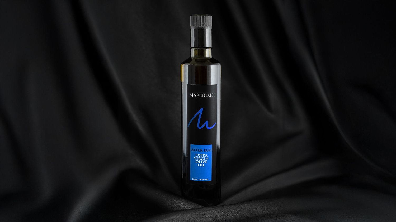 Bottle of Marsicani Extra Virgin Olive Oil displayed against dark black satin fabric background.