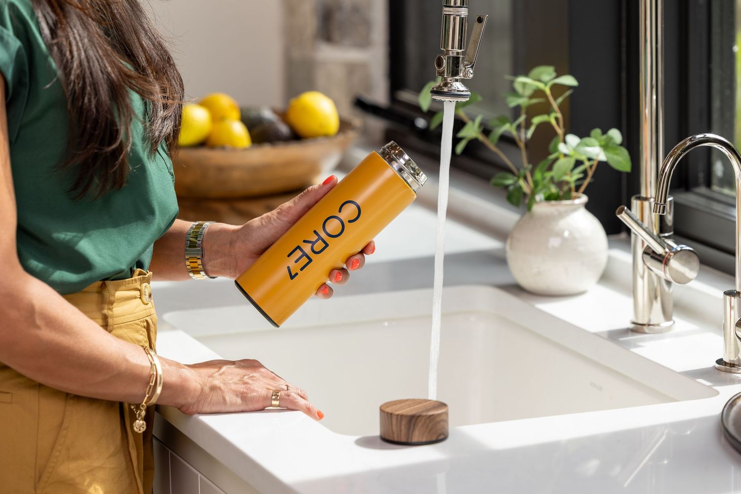 Woman filling an orange CORE hydration water bottle at a modern kitchen sink.