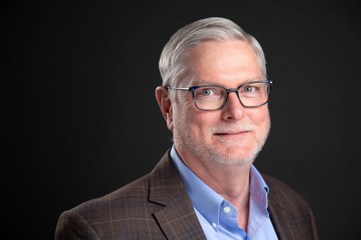 Professional headshot of mature man with glasses in brown blazer.