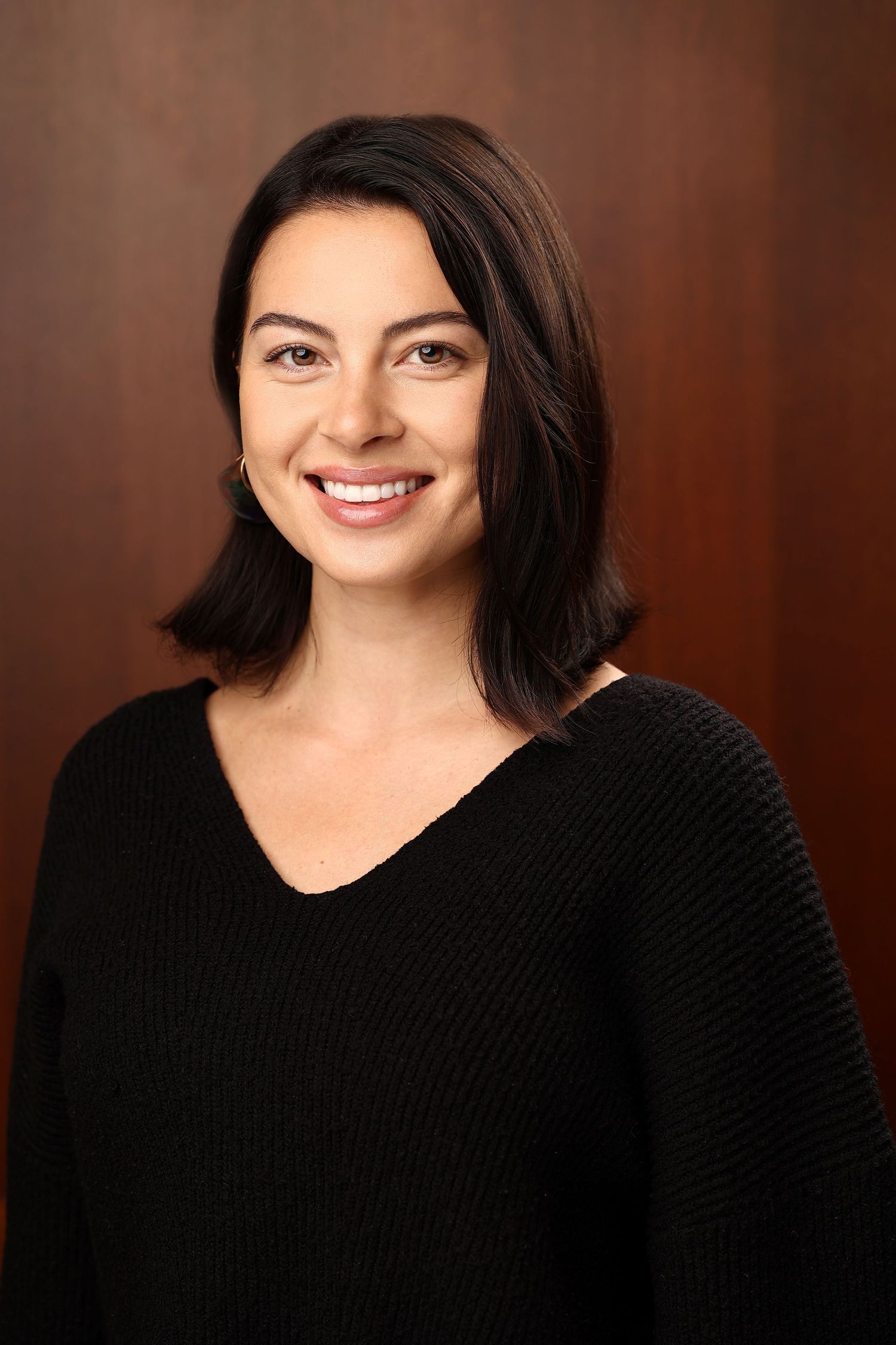 Professional headshot of a young woman with dark shoulder-length hair wearing a black v-neck sweater.