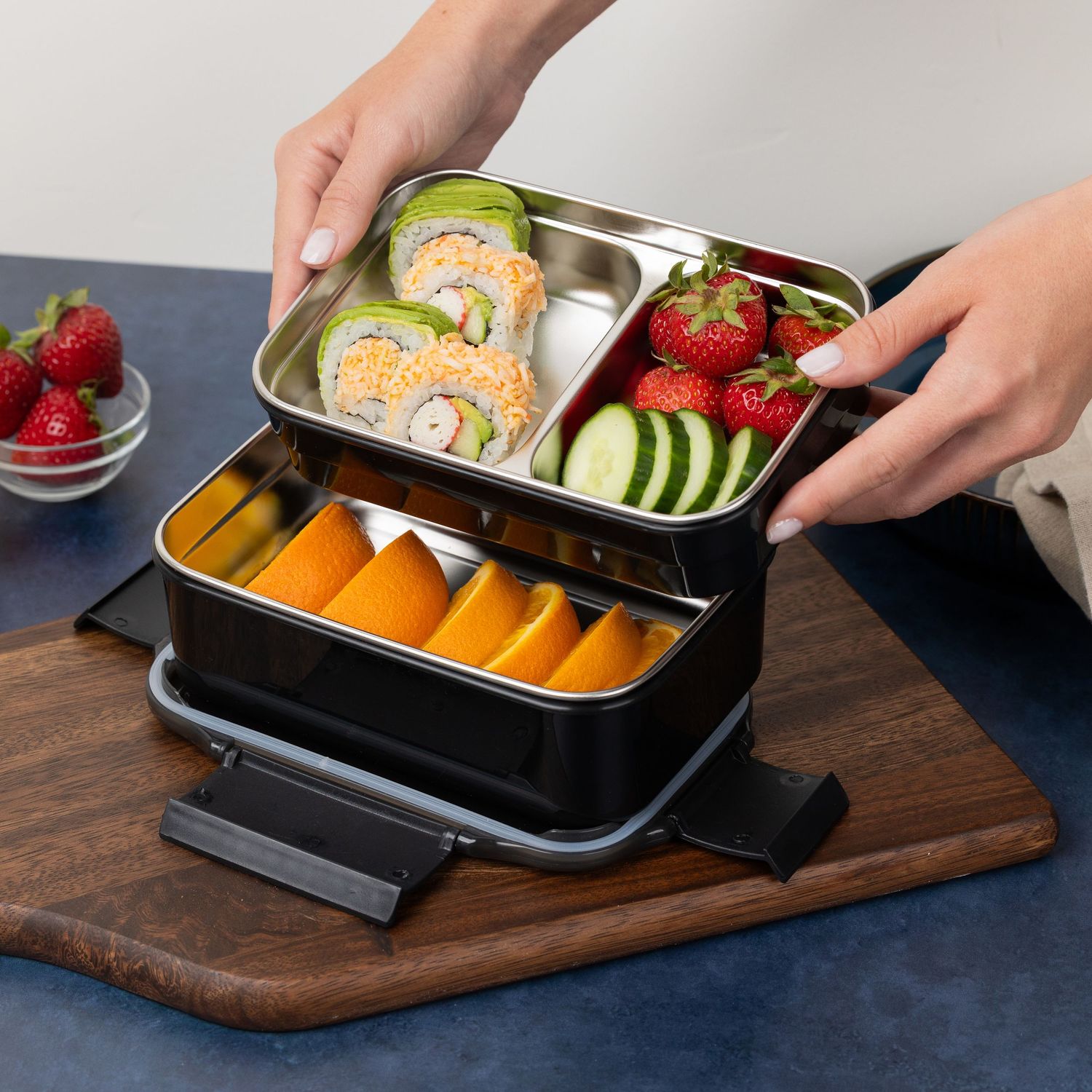 Two-tier stainless steel bento lunch box filled with sushi rolls, fruit, and vegetables.
