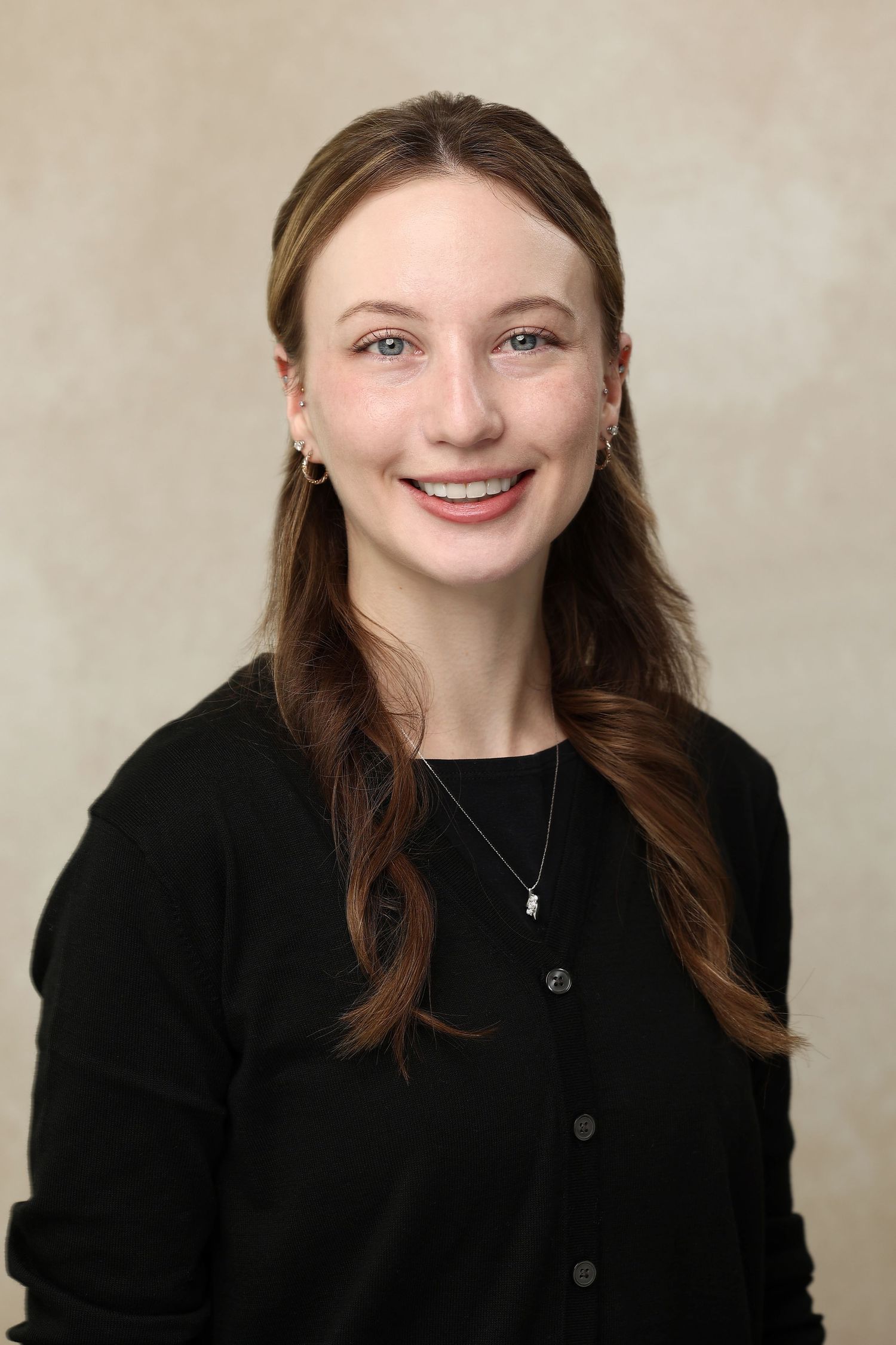 Young woman with auburn hair in black cardigan smiles for professional headshot portrait.