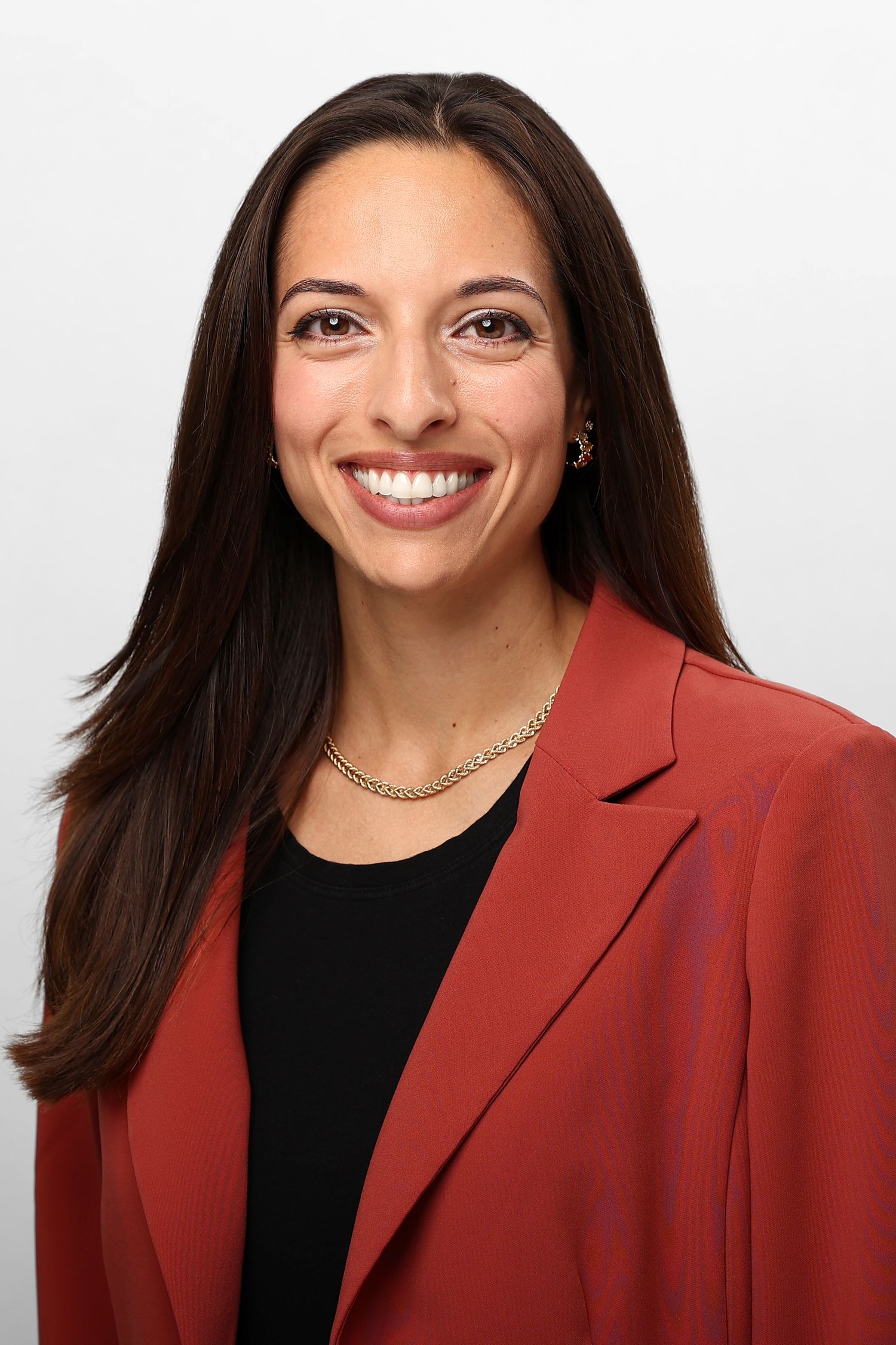 Professional headshot of a smiling woman with long dark hair in a red blazer and gold necklace.
