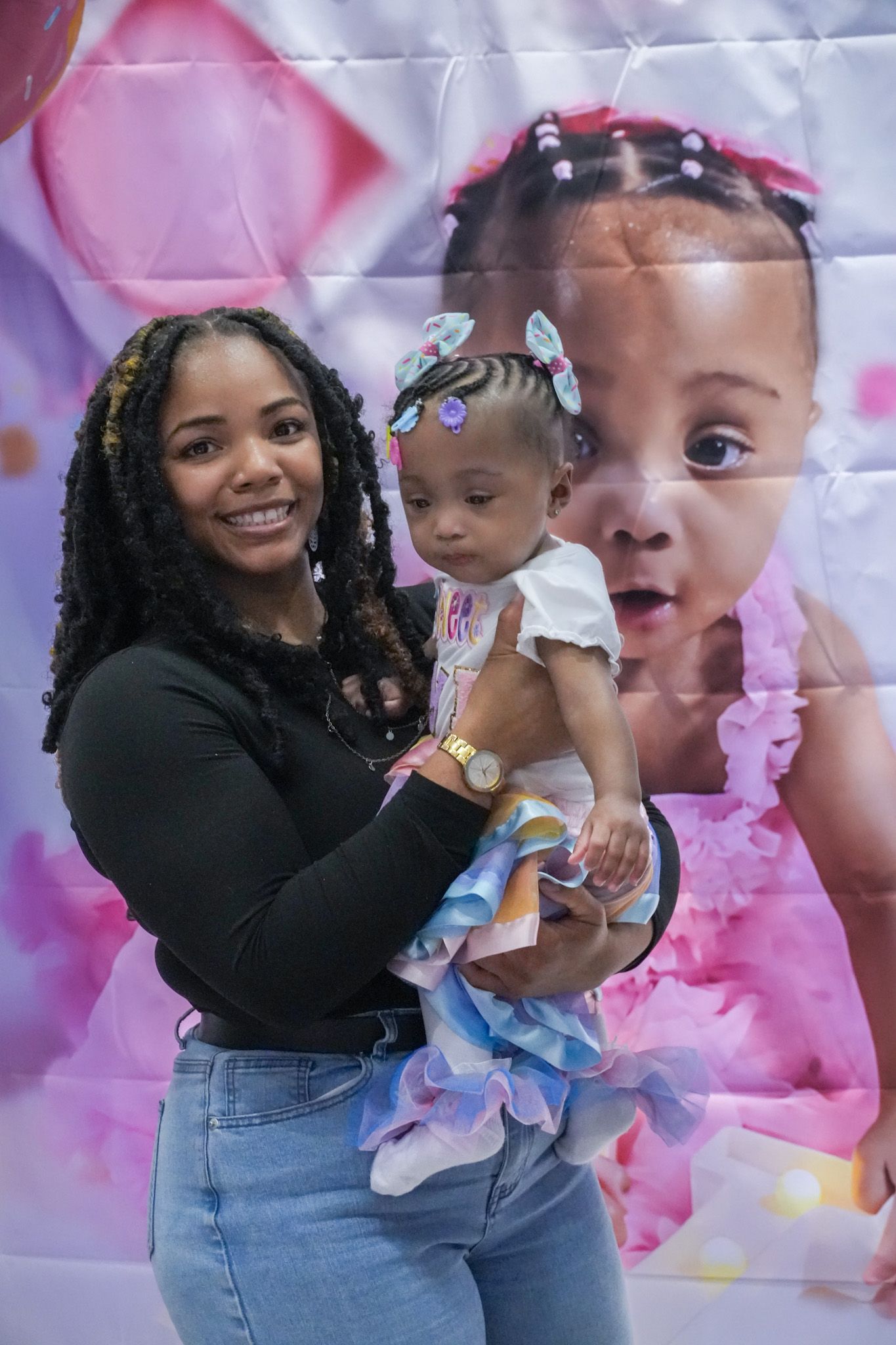 Smiling young mother holding her baby girl at a pink-themed birthday party celebration.