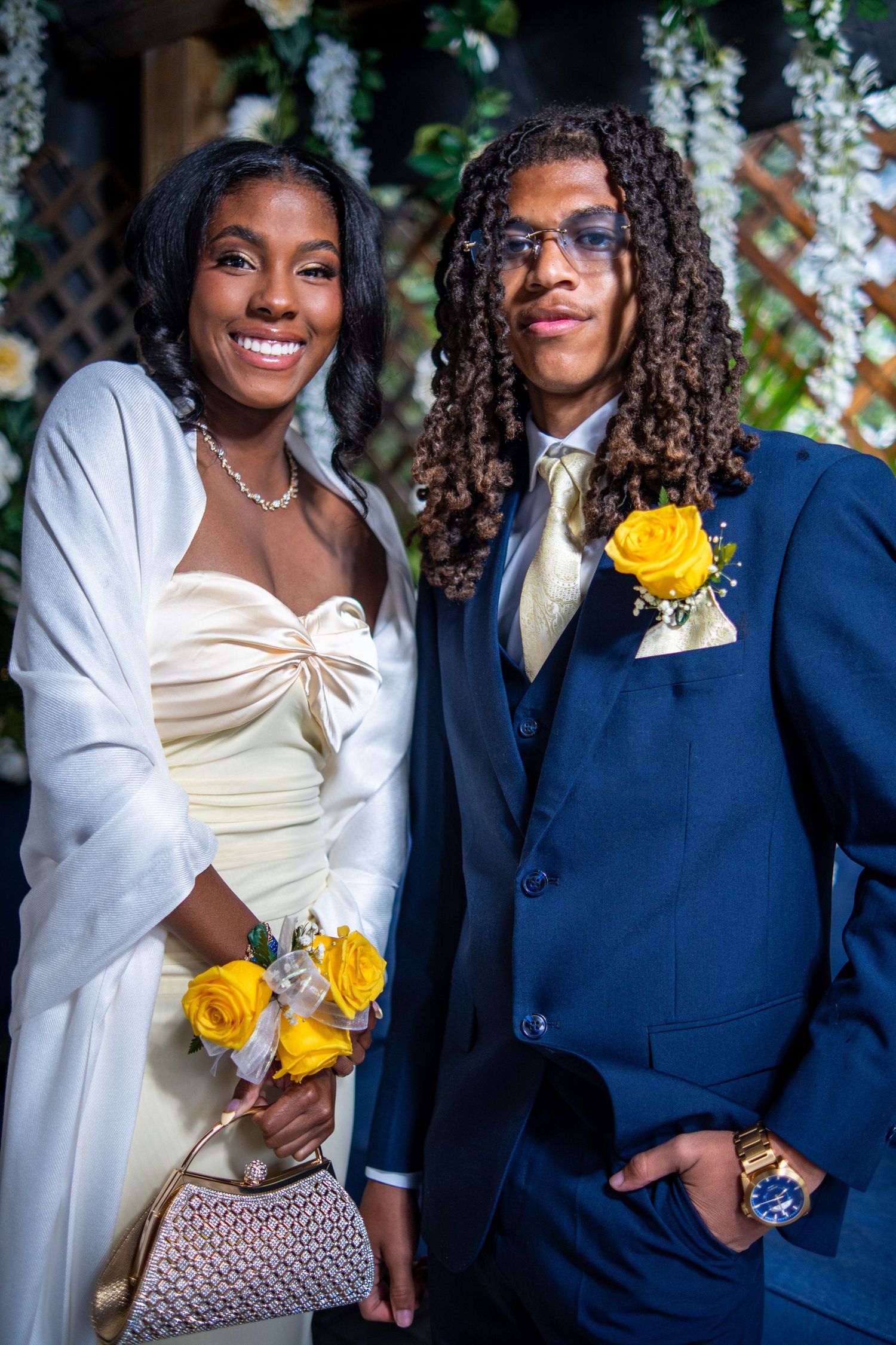 Prom couple in coordinating gold and navy formal wear pose with yellow rose corsages and bouquet.