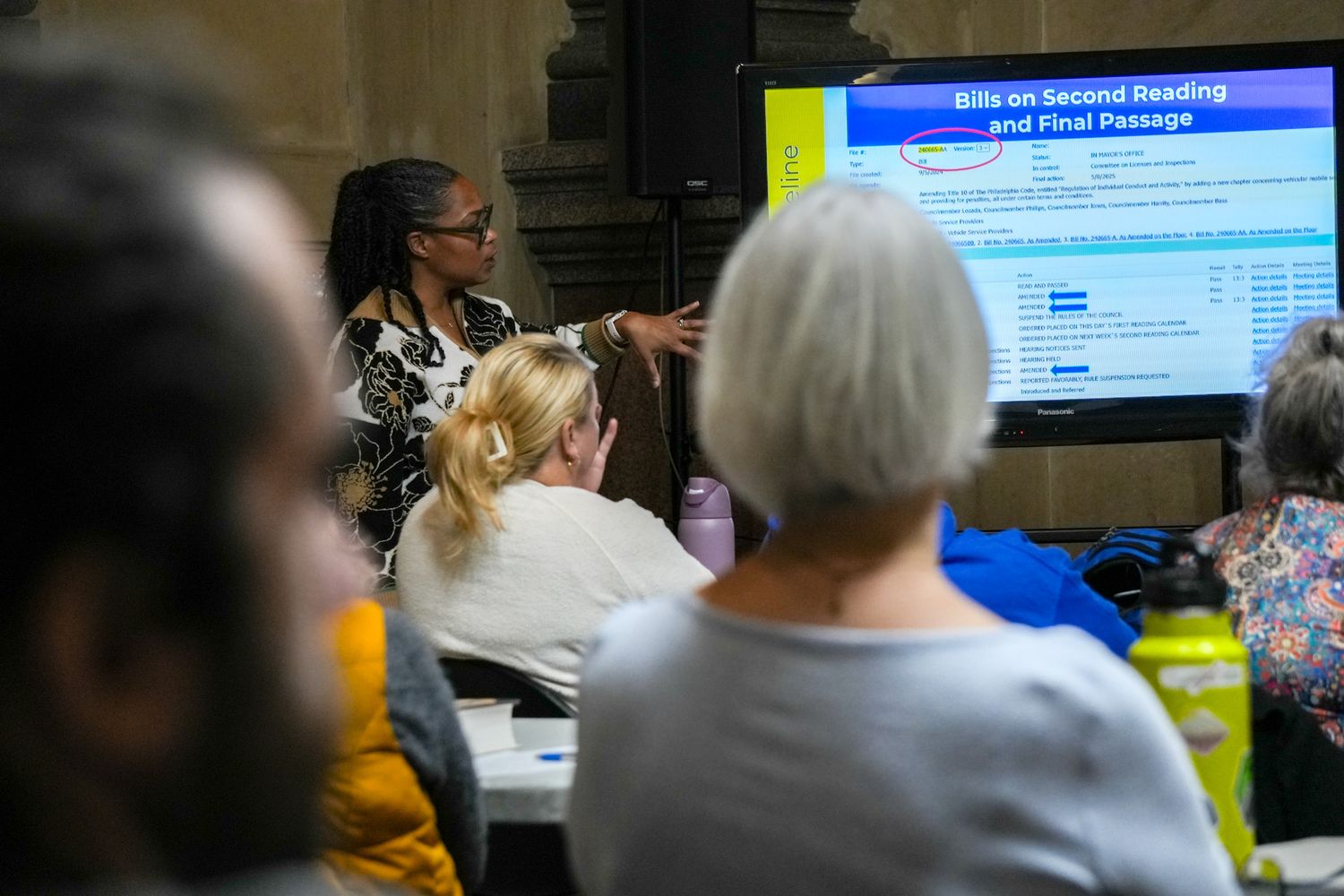 Woman presenting Bills on Second Reading slide to a group of seated attendees in a meeting room.