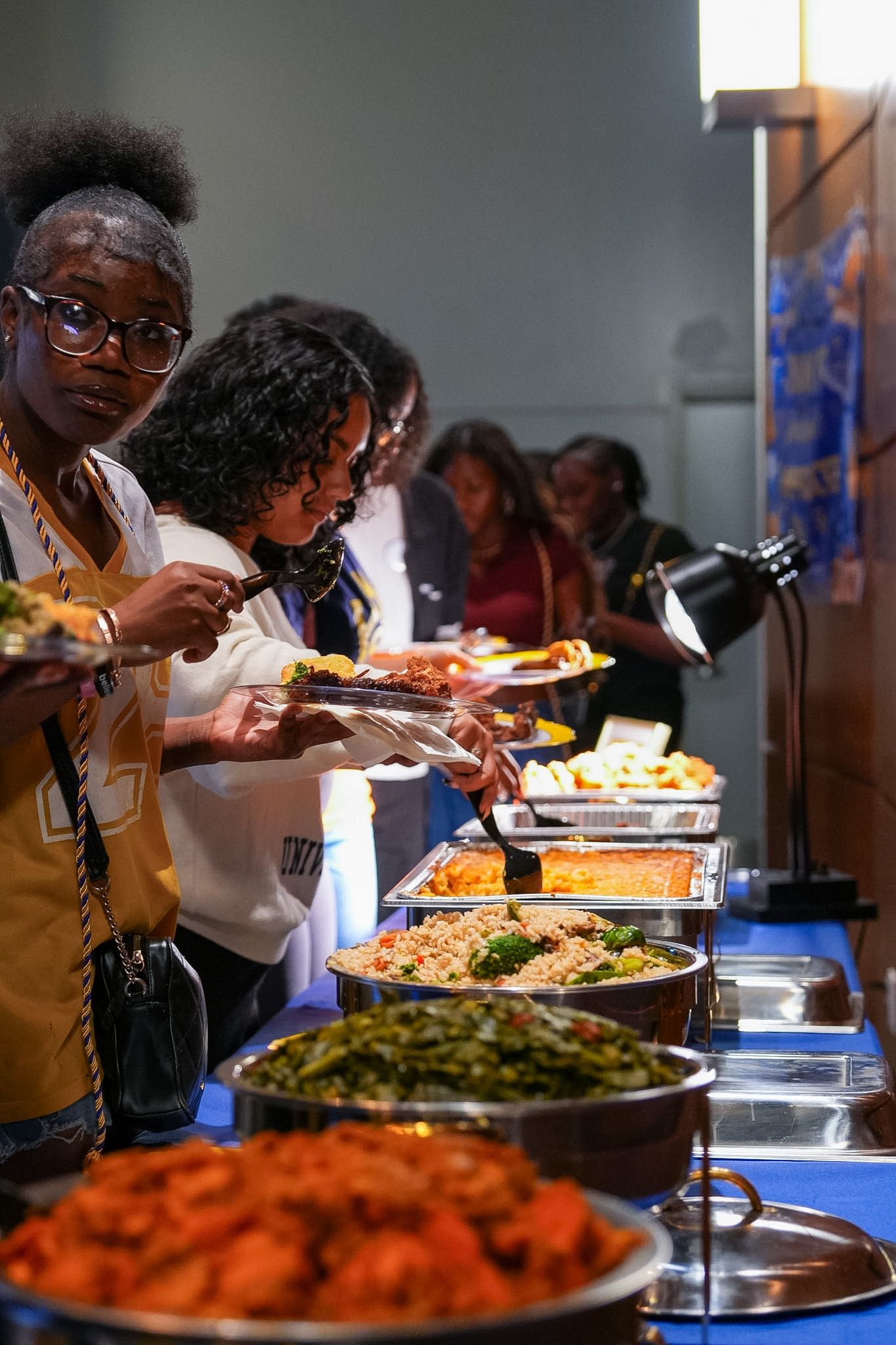 People serving themselves at a buffet line with various colorful dishes at a catered event.
