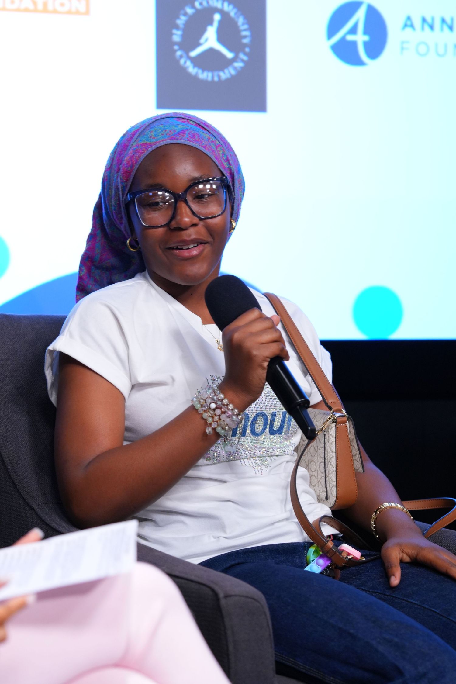Woman in colorful hijab and glasses speaks into microphone at panel event with Jordan Brand and Annenberg Foundation logos.