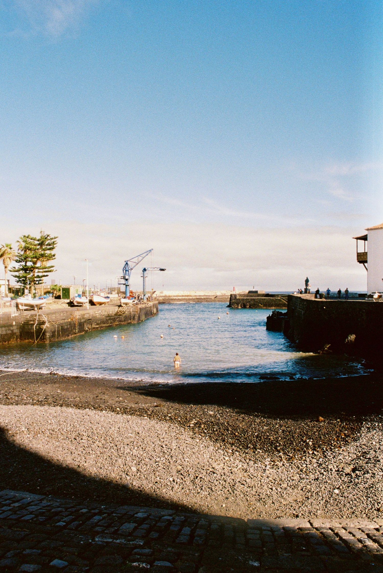 Rocky coastal shoreline with seawall and buildings visible against clear blue sky.