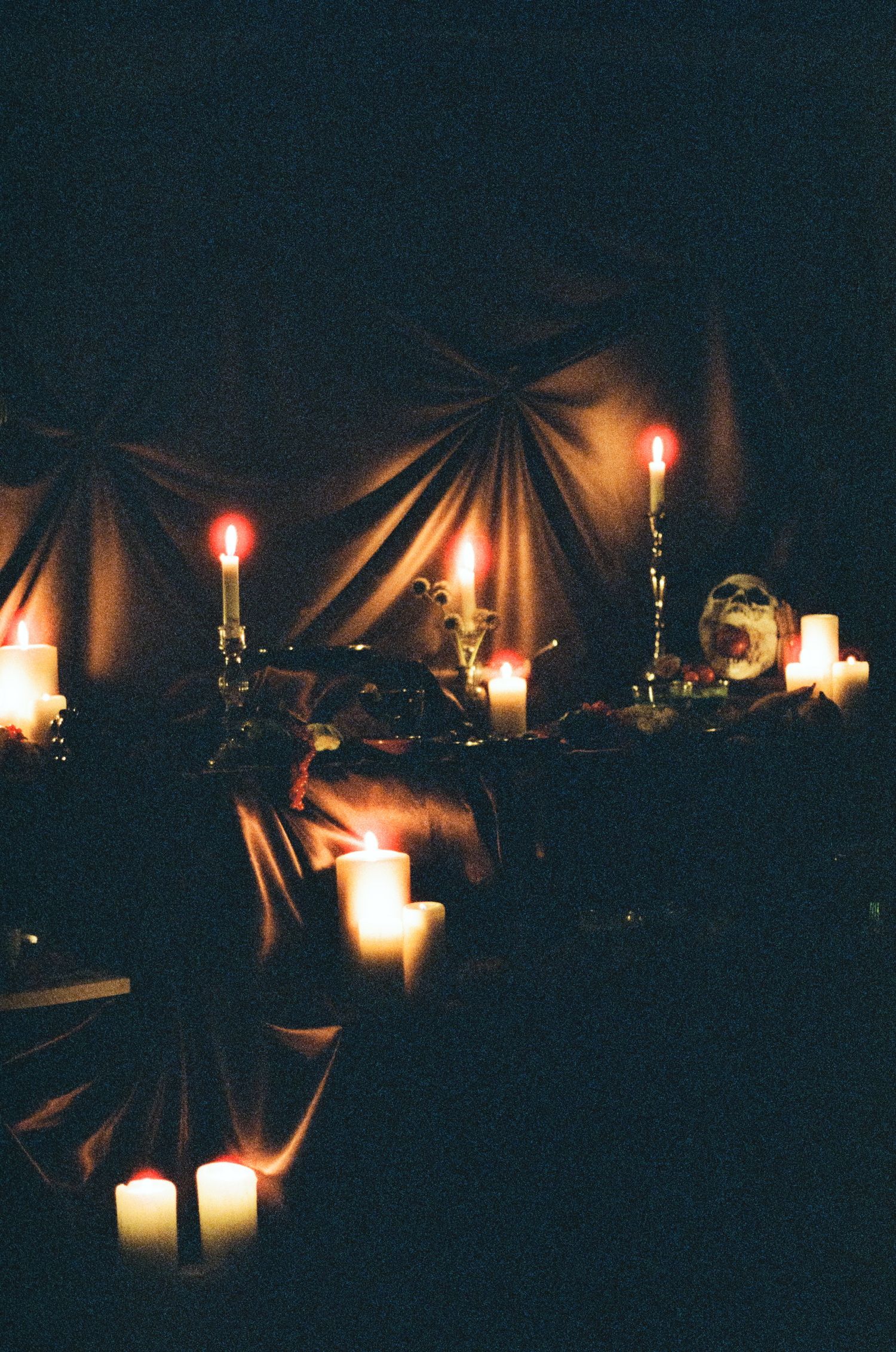 Dramatic candlelit Halloween table setting with draped fabric backdrop.