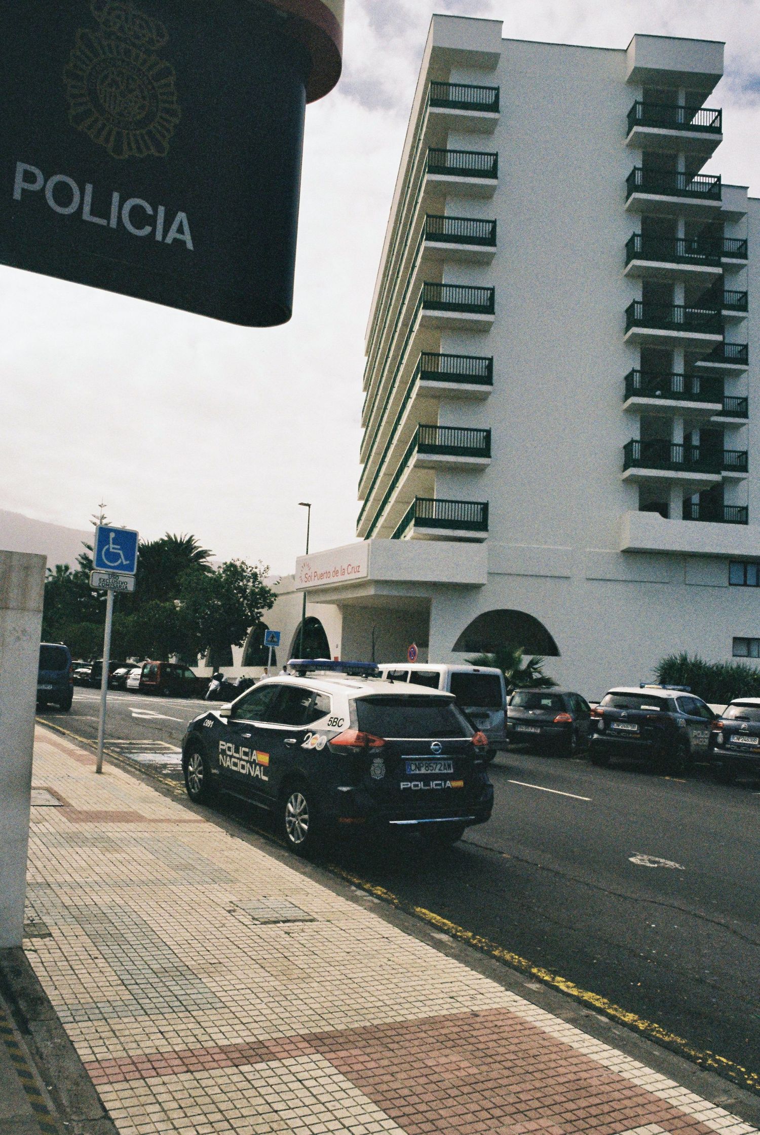 White apartment building with police signage and parked cars on tiled parking area.