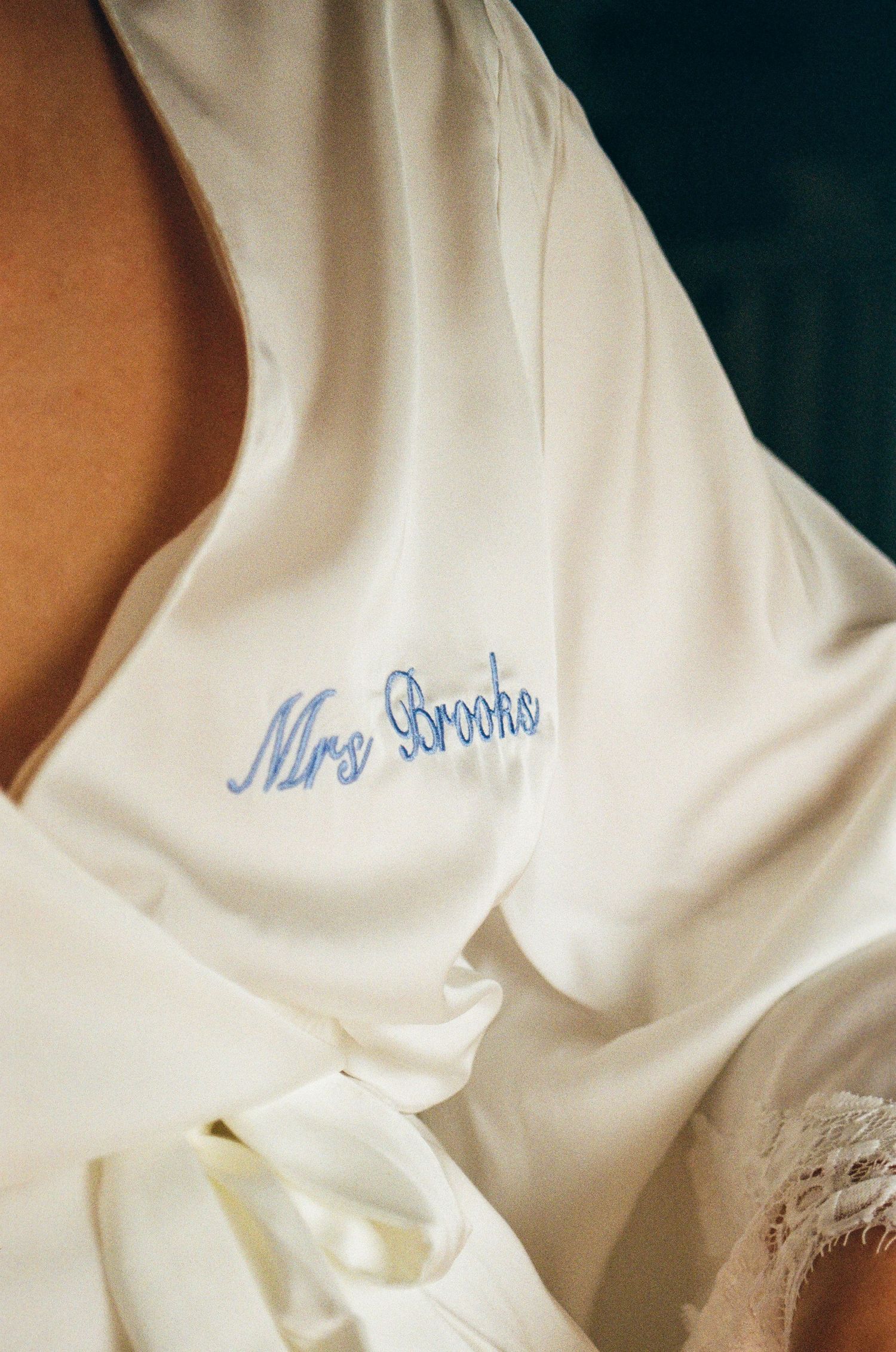 Close-up detail of white silk wedding robe with blue embroidered text.