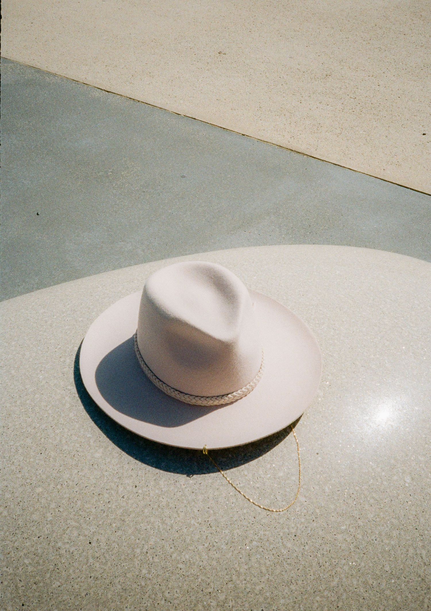 Minimalist photo series of white hat casting shadows on light concrete surface.