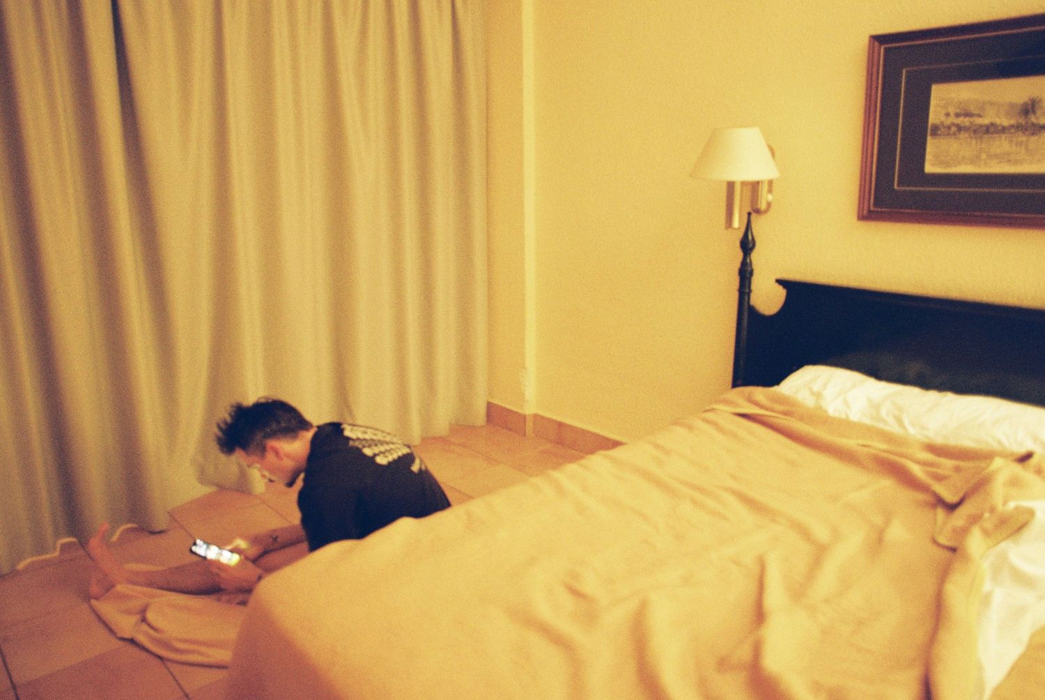Dimly lit hotel room with a bed and someone using a device while lying down.