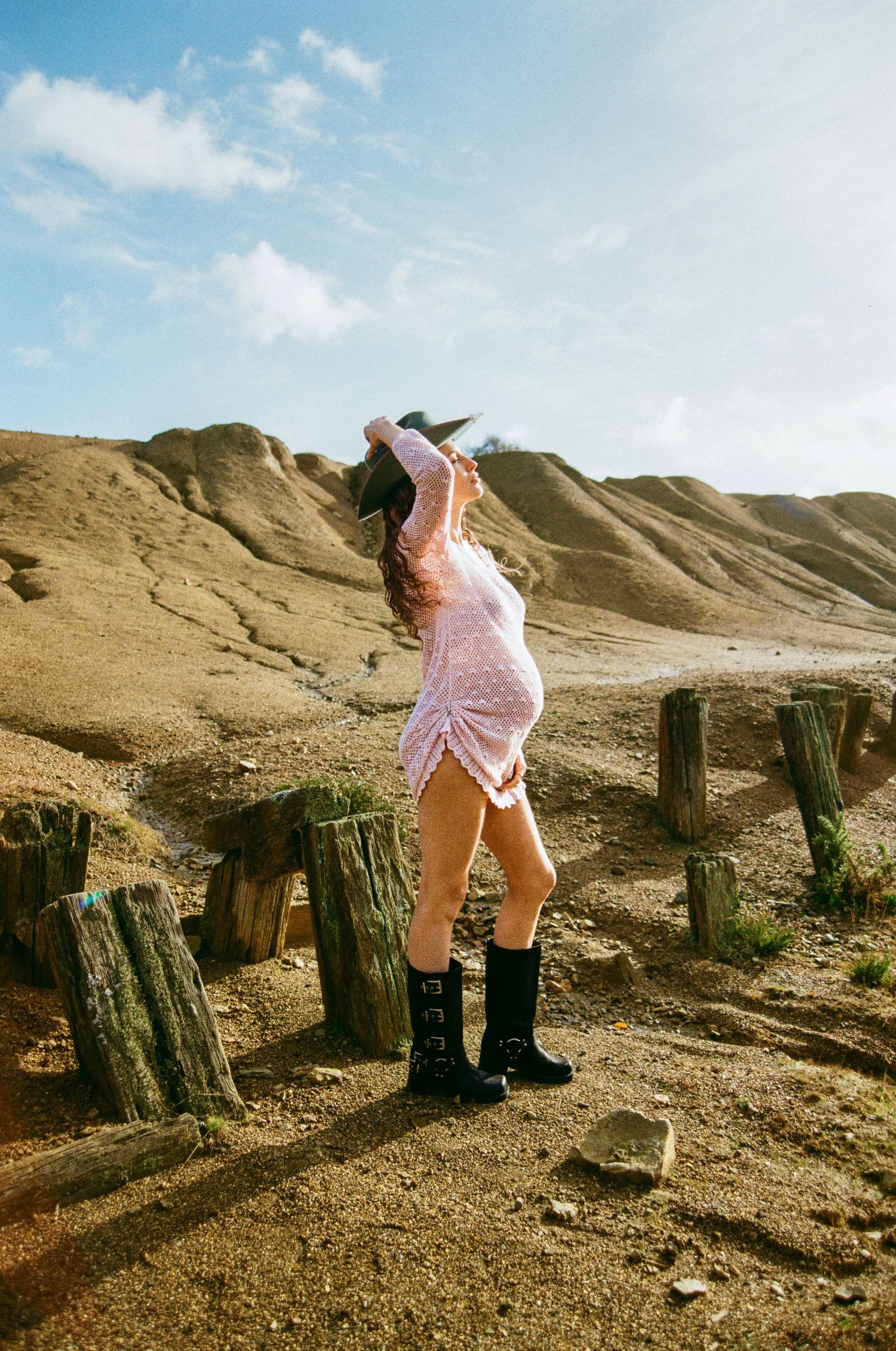 Figure in pink dress and boots posing dramatically against desert rock formations.