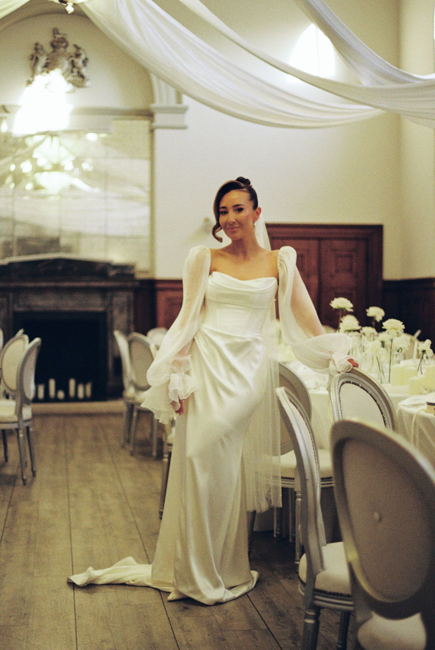 Elegant wedding dress in ivory silk with a fitted silhouette and draped fabric details shown in a room with white decor.