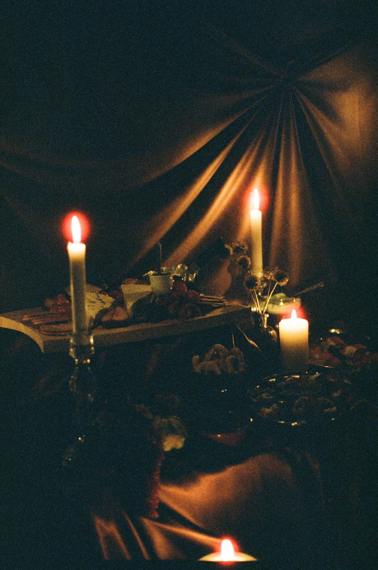 Multiple candles illuminate a dark room with soft warm light casting shadows on surrounding objects.