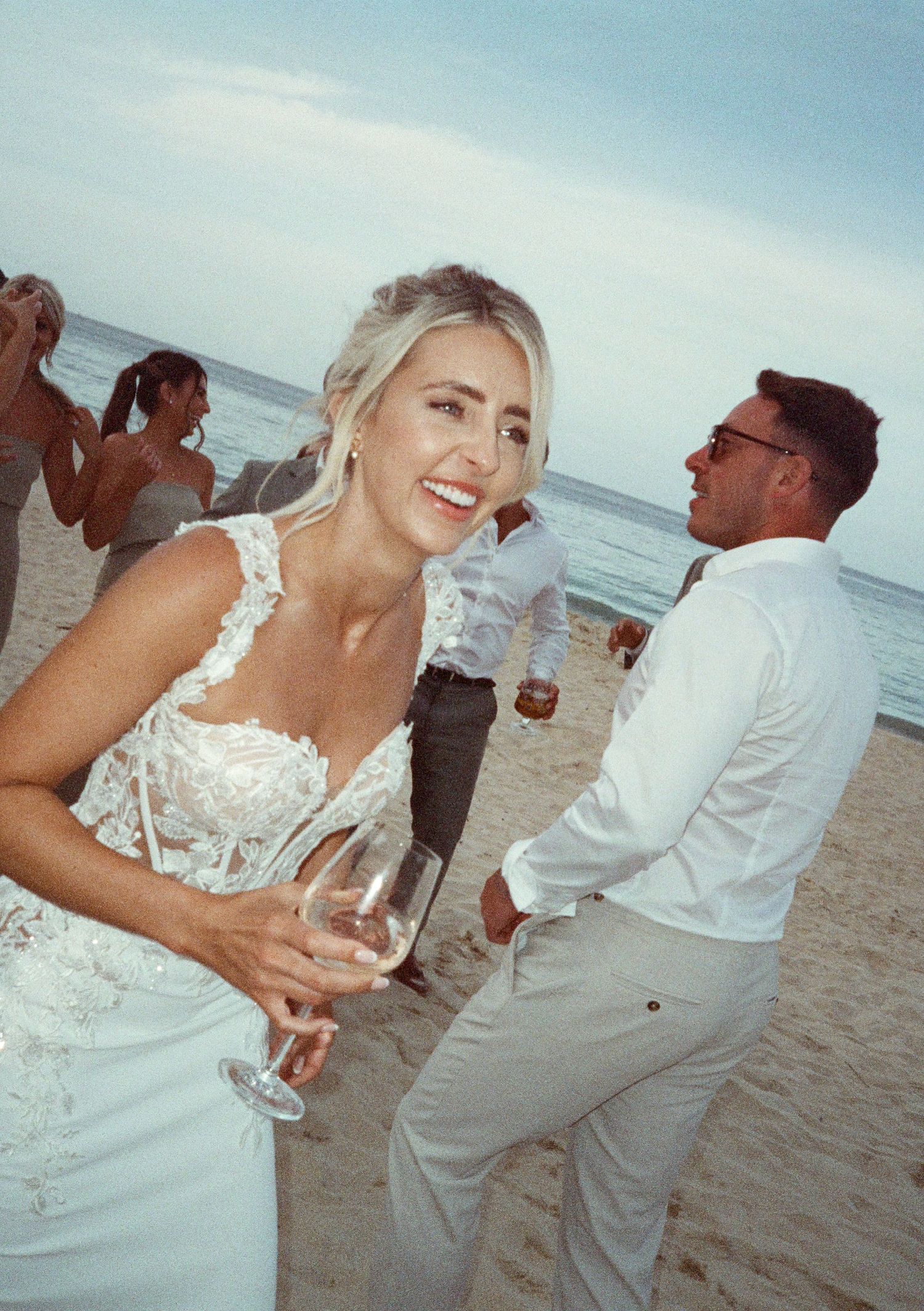 Joyful celebration on a beach with people in white attire dancing and having fun.