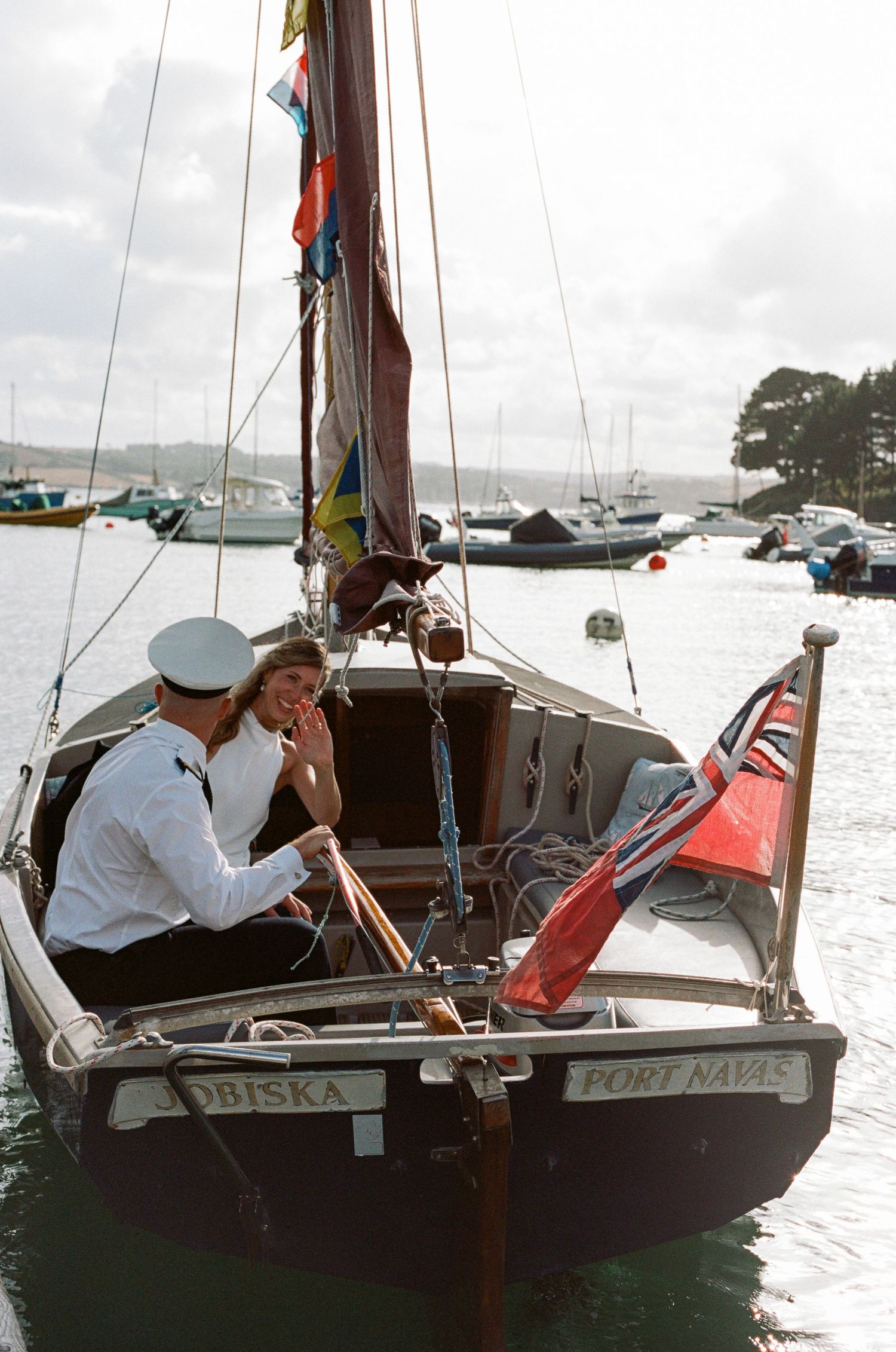 A couple shares an intimate moment aboard a sailboat decorated with colorful flags in a harbor.