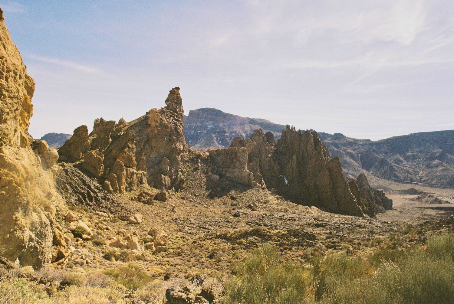 Panoramic view of desert rock formations and mountains against bright sky.