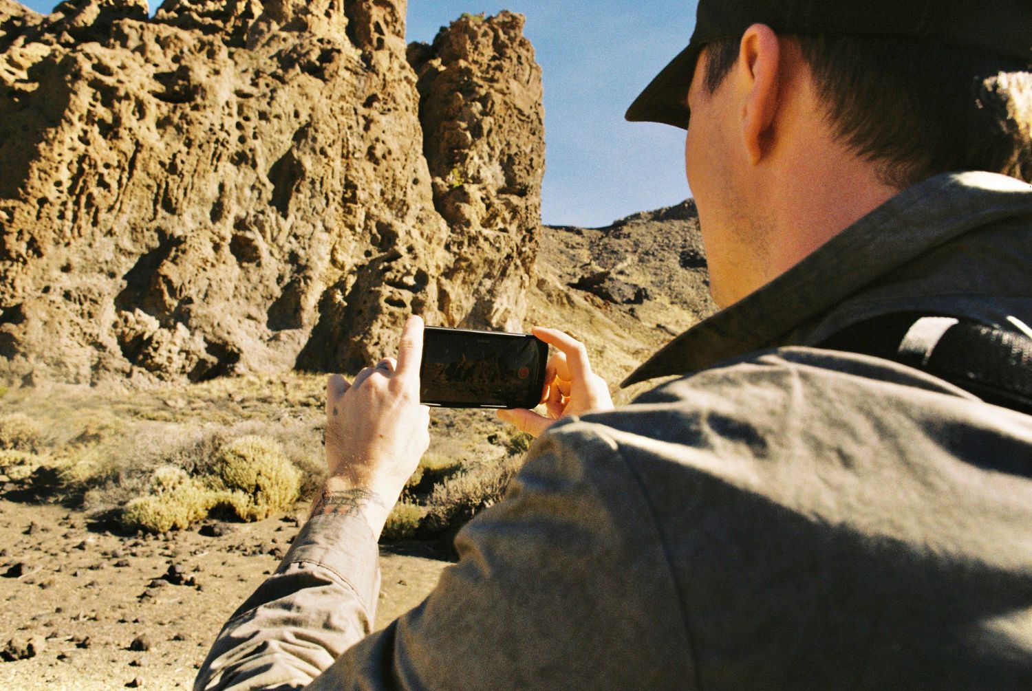 Someone taking a photo of rocky desert cliffs with a smartphone on a sunny day.