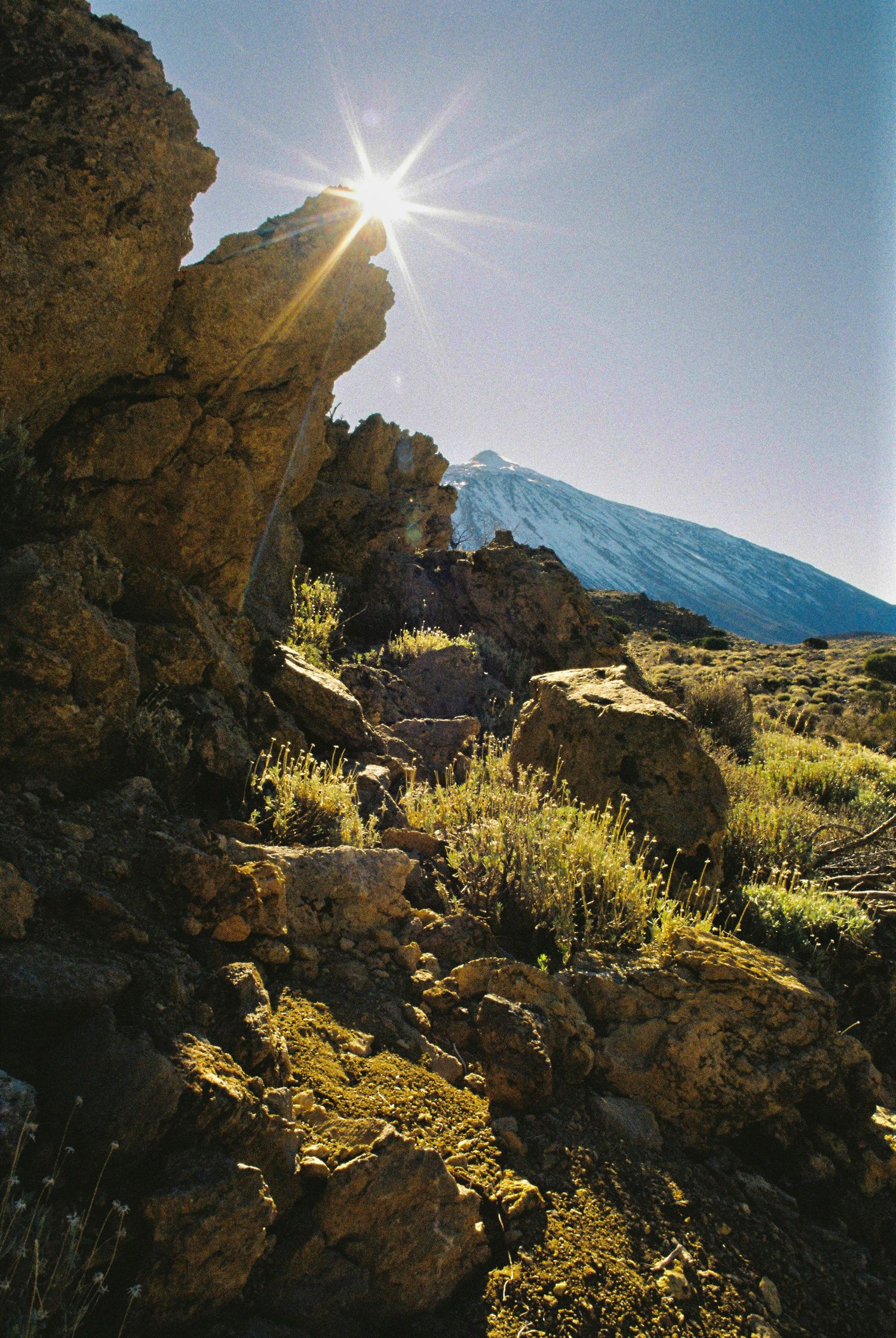 Sunlit rocky cliffs and vegetation with mountain peaks visible in the background.