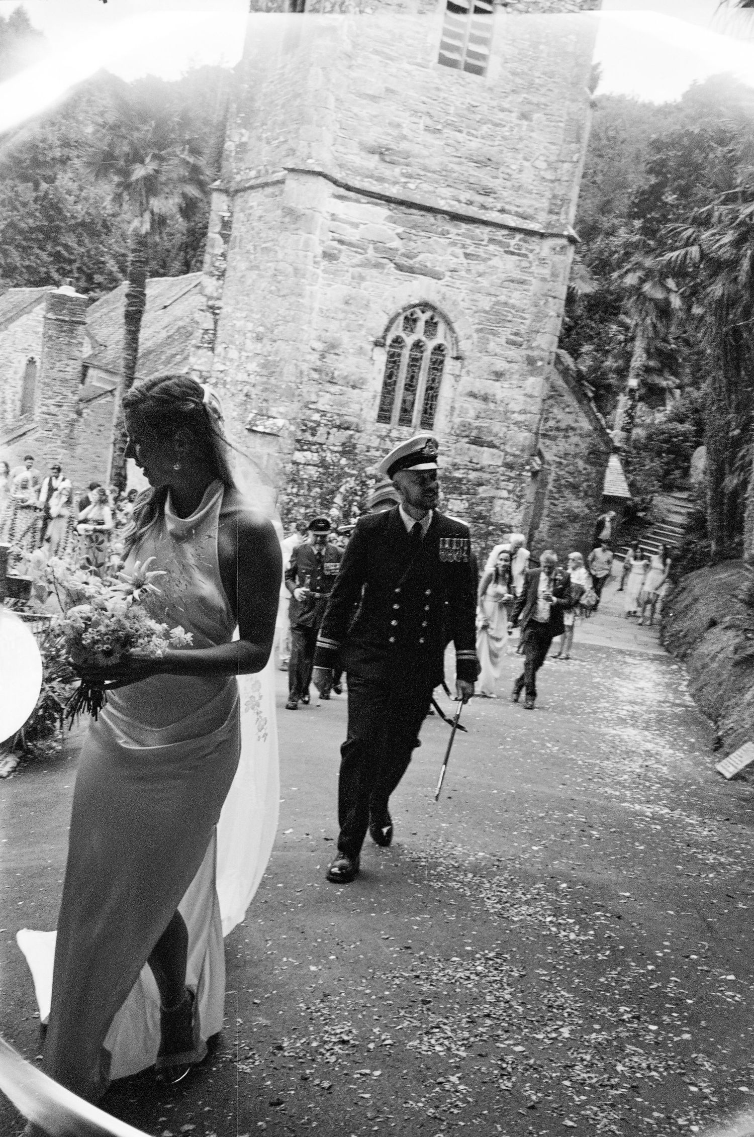 Black and white photo of wedding guests dancing outdoors near historic stone church building.
